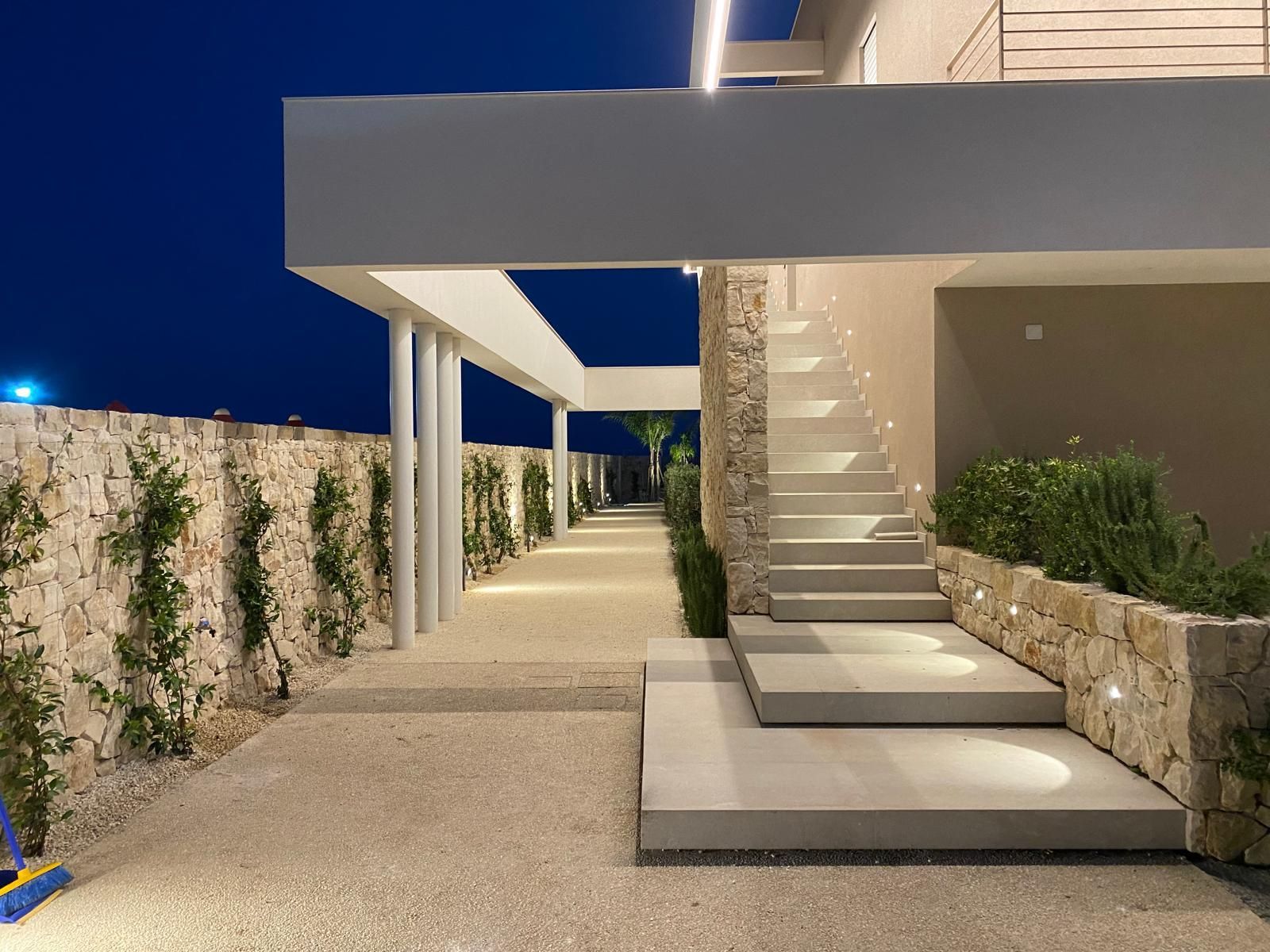 Passeggiata notturna all'aperto con muri in pietra, scale e una moderna tenda illuminata sotto un cielo scuro