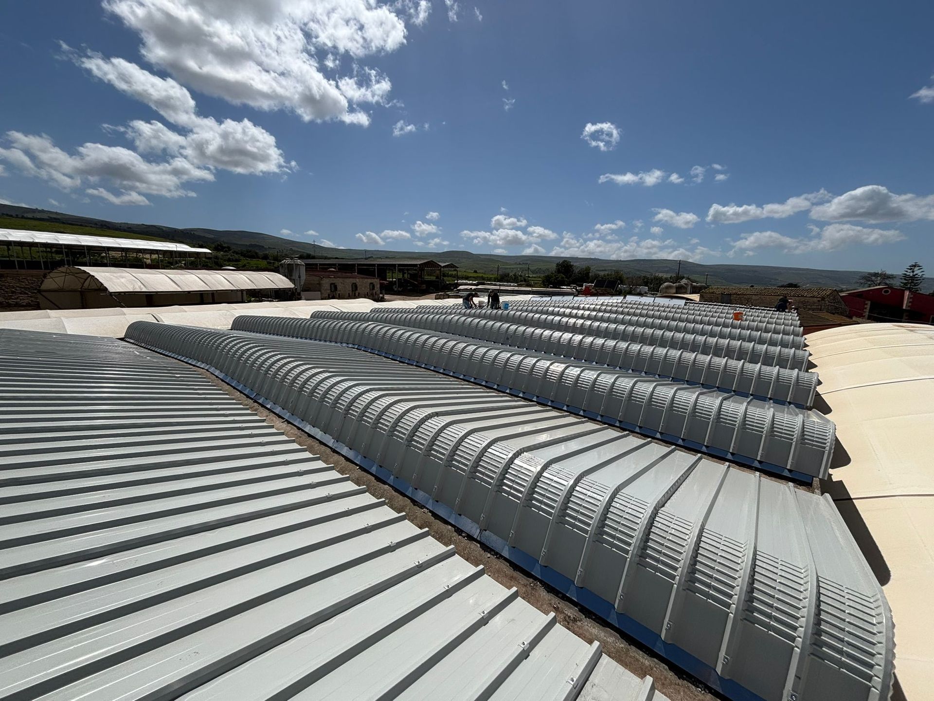 File di condotti di ventilazione argentati sui tetti sotto un cielo azzurro nuvoloso