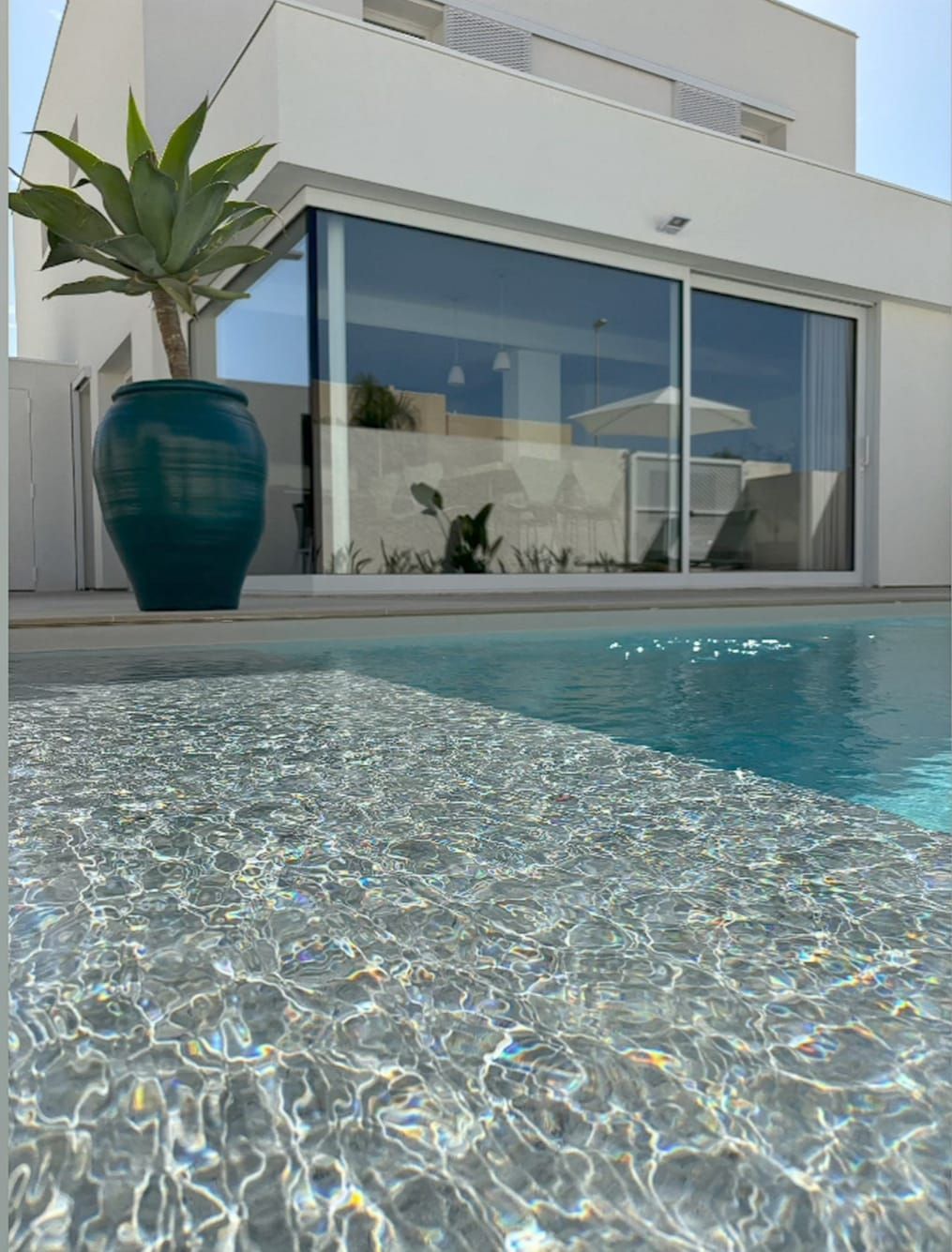 Casa moderna con parete in vetro accanto a una piscina scintillante e grande fioriera blu.
