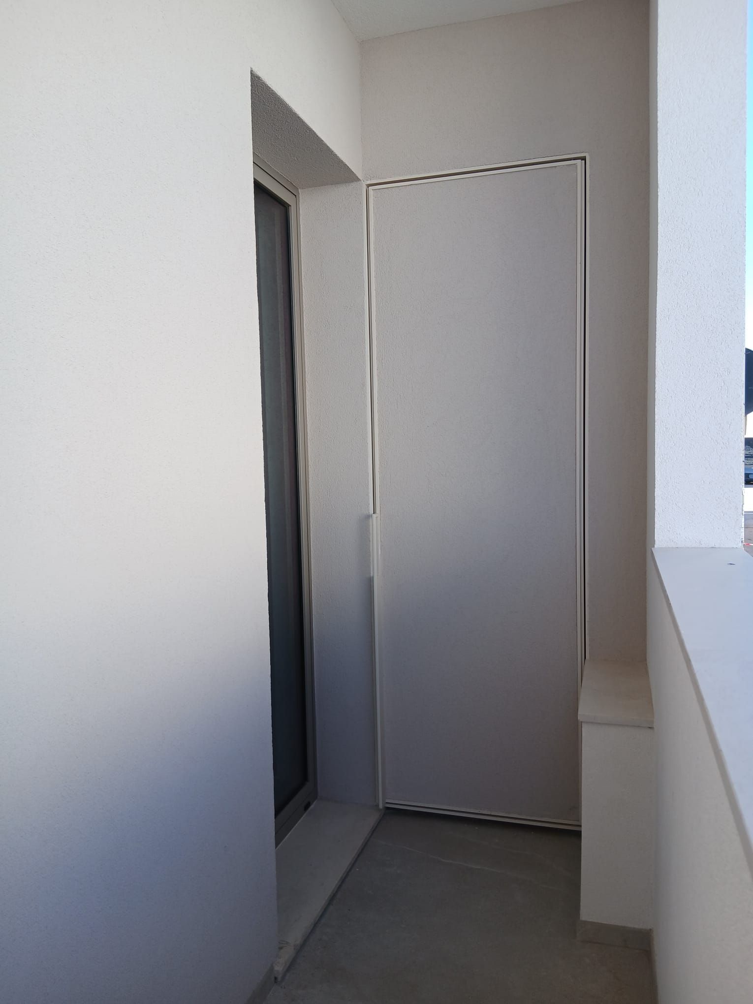 Stretto corridoio con balcone bianco, con porta chiusa e ringhiera sulla destra.