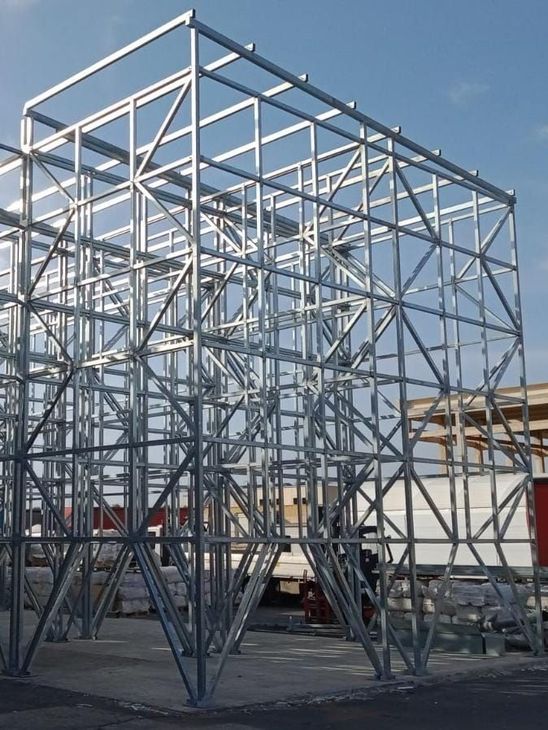Operai su una piattaforma elevatrice assemblano una struttura in acciaio su un cantiere in cemento sotto un cielo grigio.