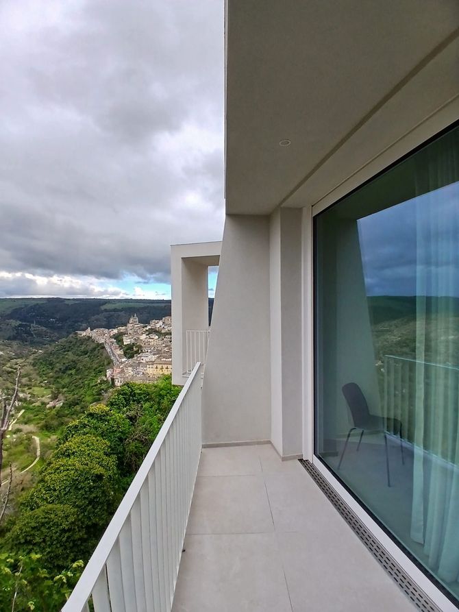 Balcone adiacente a un'ampia porta scorrevole in vetro con tende verdi e vista sulla città.