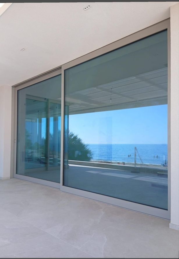 Soggiorno moderno con divano bianco, ampia finestra e porte scorrevoli in vetro che conducono al patio.