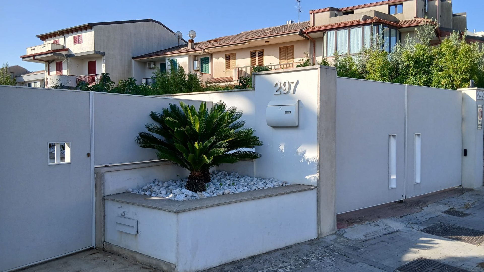 Casa d'angolo in stucco bianco con una piccola fioriera e una palma, situata in una strada residenziale.