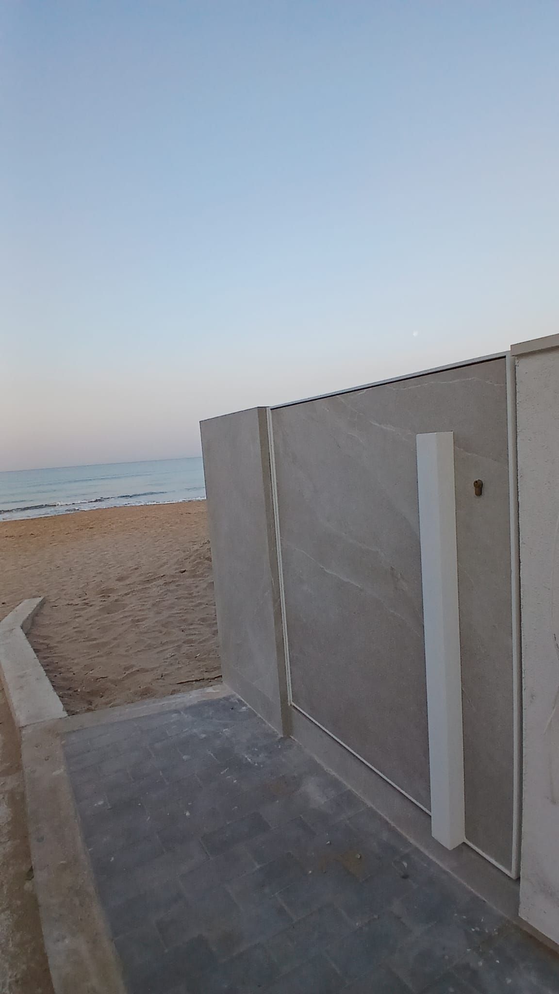 Passeggiata deserta sul lungomare, accanto a un muro di cemento grigio, sotto un cielo limpido.