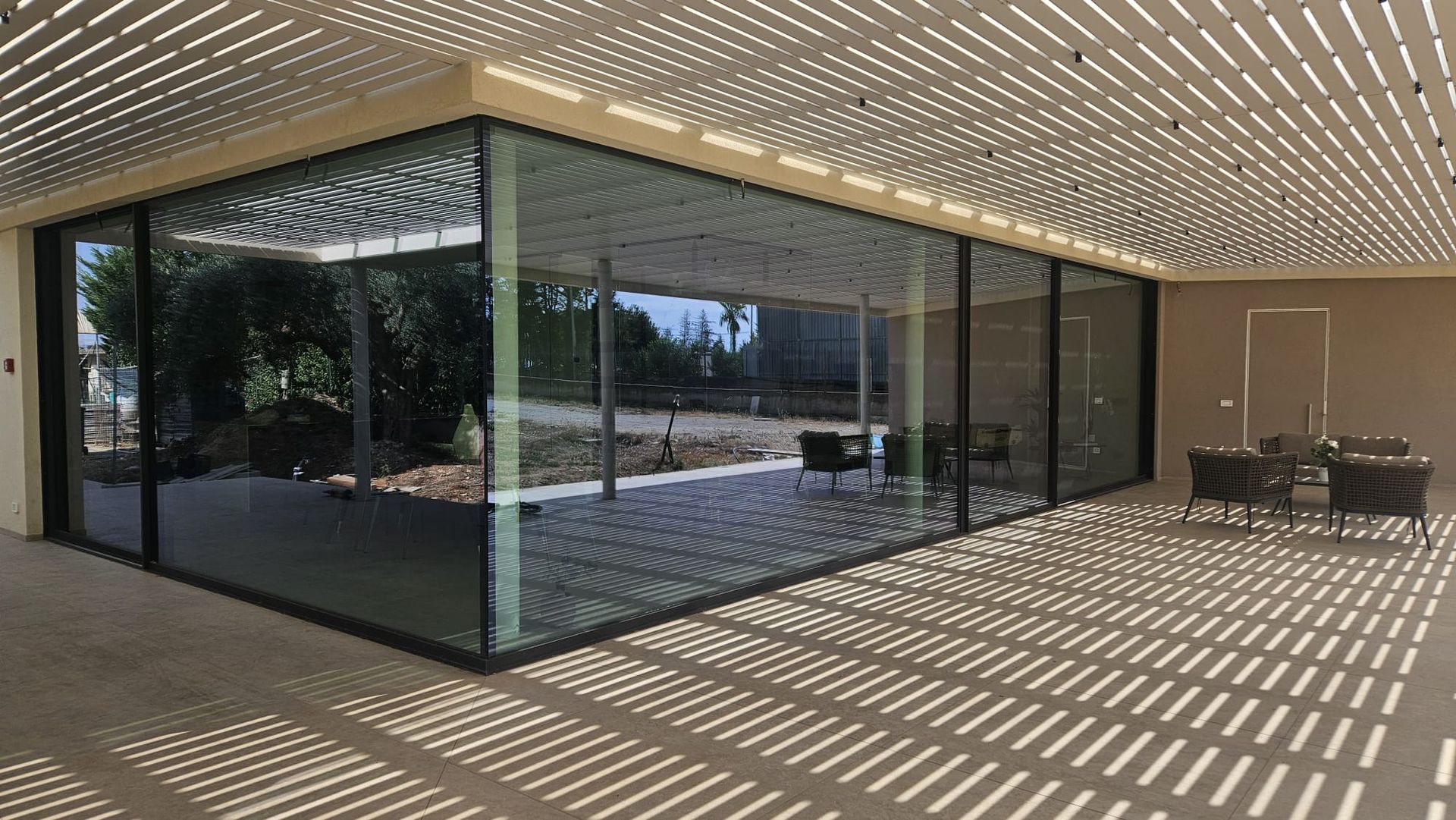 Moderno edificio in vetro con tettoia a lamelle e una piccola roccia in primo piano.
