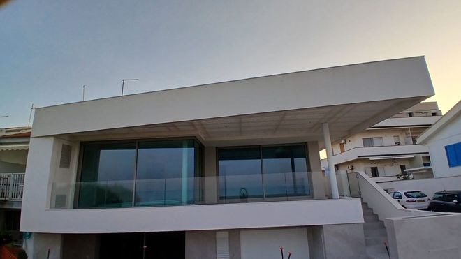 Piccola cucina con carta da parati a motivi blu, finestra, piano di lavoro e mobile bianchi; piante e fiori fuori dalla finestra.