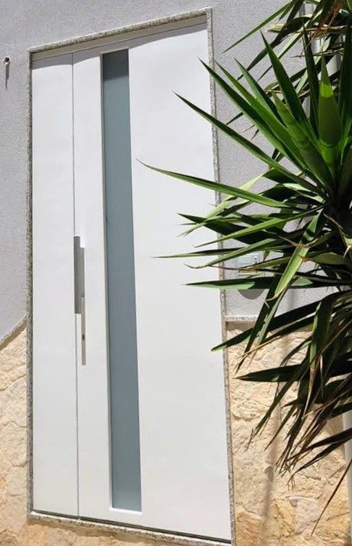 Porta d'ingresso bianca con un pannello stretto in vetro satinato accanto a un muro in pietra e piante