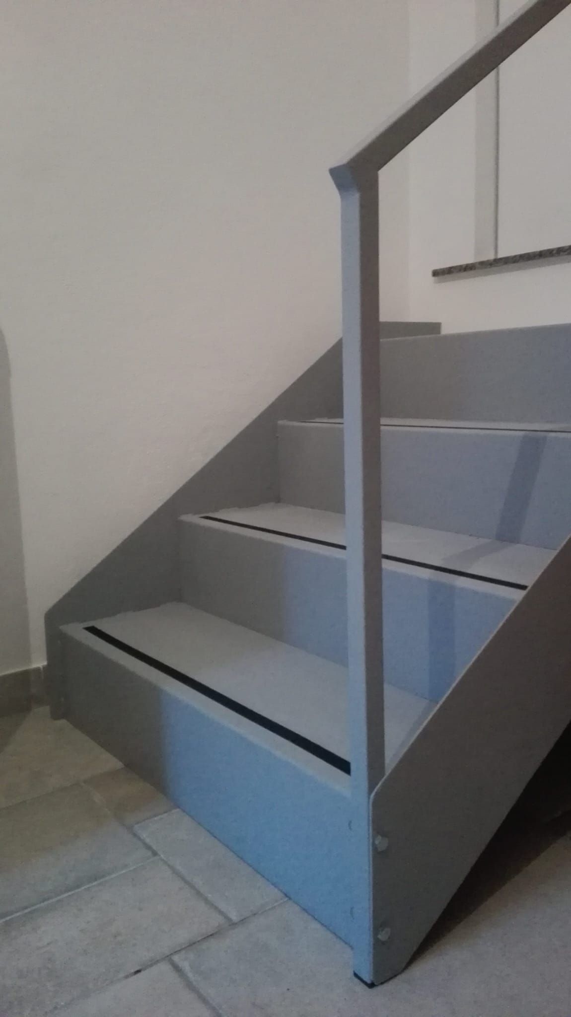 Scala interna grigia con corrimano in metallo e base dipinta di blu su una parete bianca.