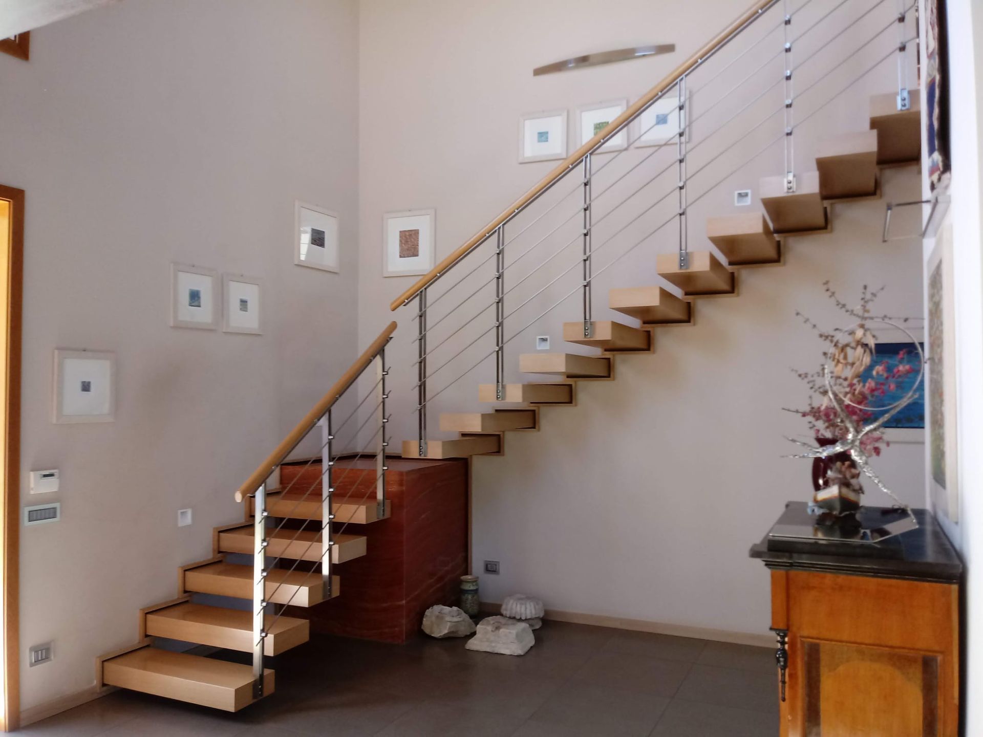 Scala moderna con gradini in legno, ringhiera in metallo e pareti beige in un interno luminoso.