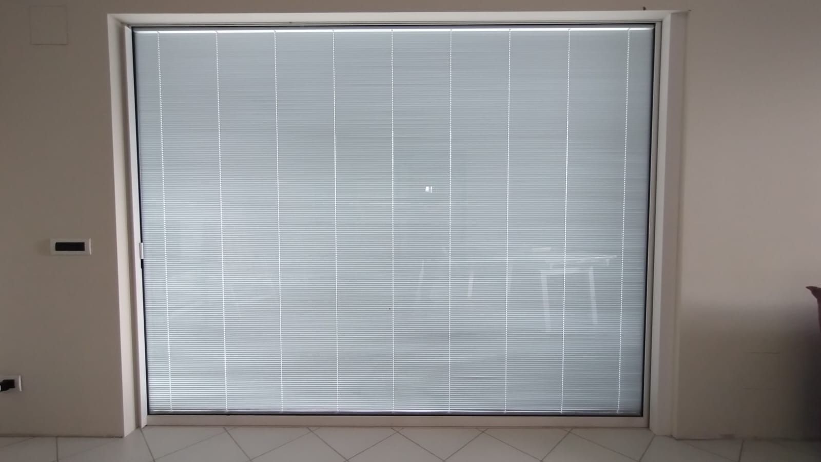 Tende bianche chiuse che coprono una porta, con pareti beige e pavimento piastrellato.