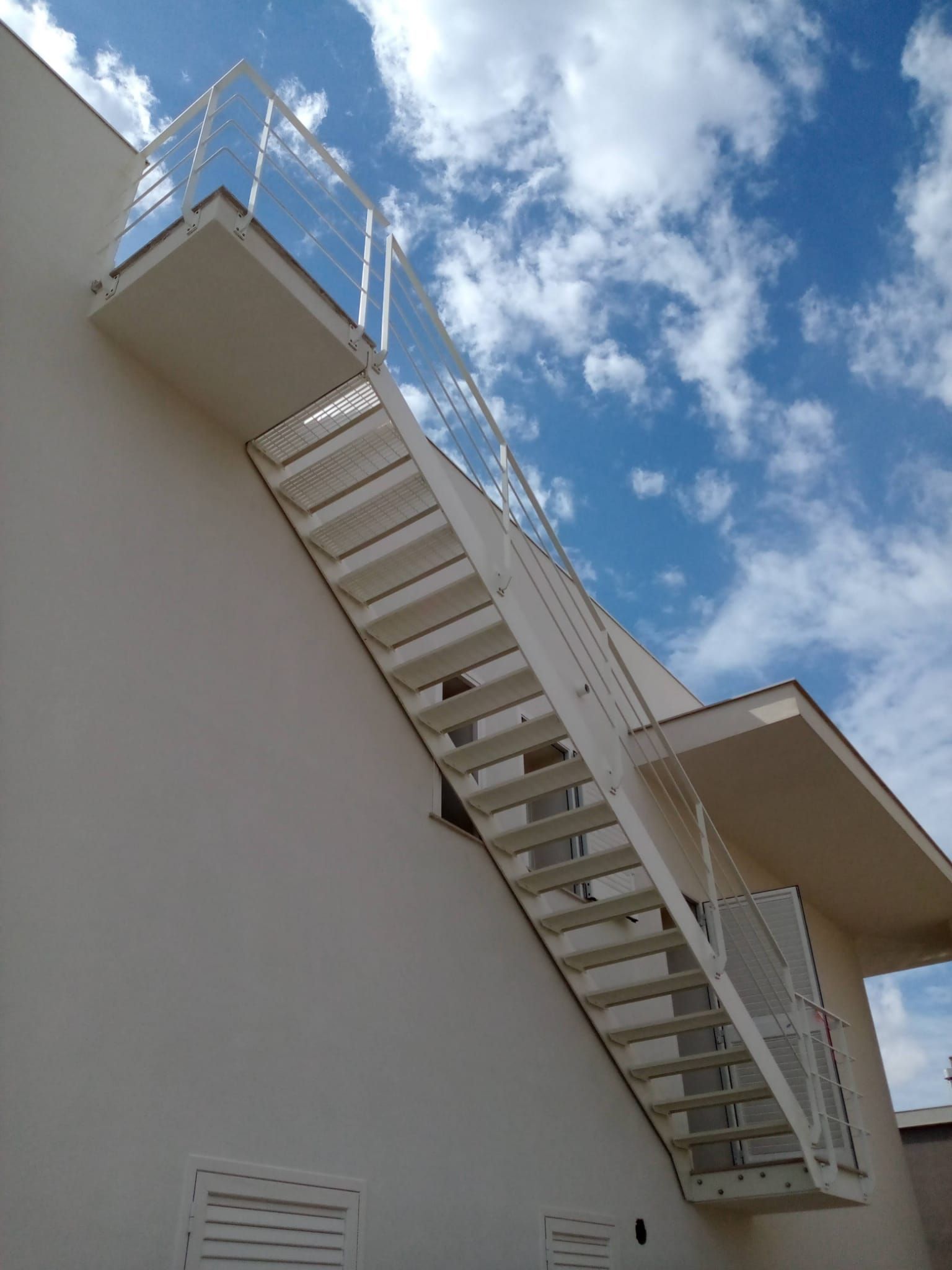Scala esterna in metallo su un edificio bianco contro un cielo blu con nuvole
