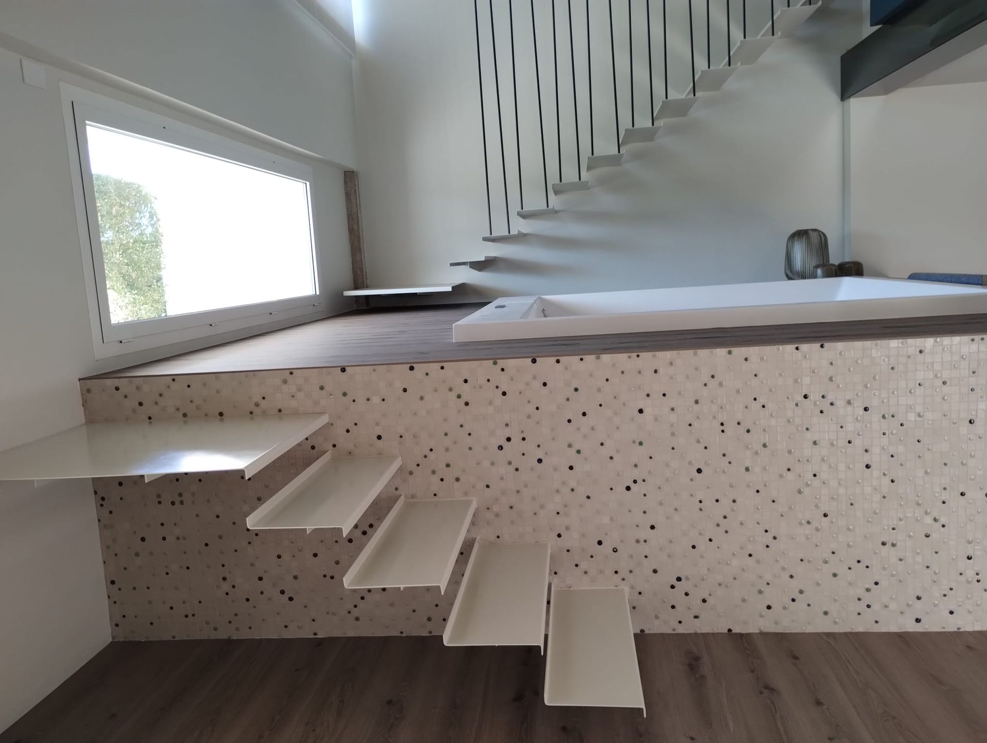 Interno minimalista bianco con una piccola scala che conduce a una piattaforma rialzata con ringhiera.