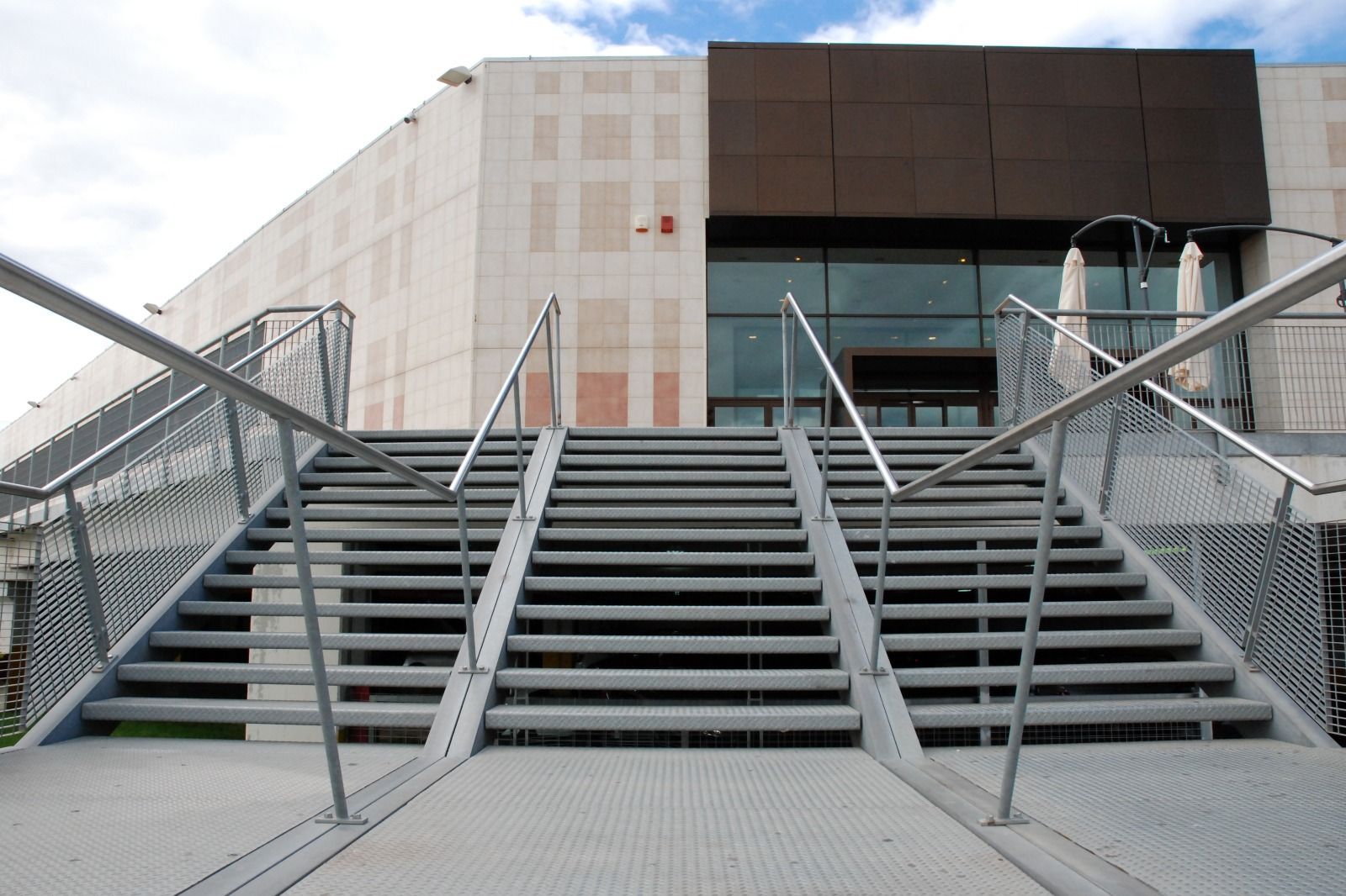 Un'ampia scala metallica conduce all'ingresso di un edificio moderno con ringhiere e parapetti in rete metallica.