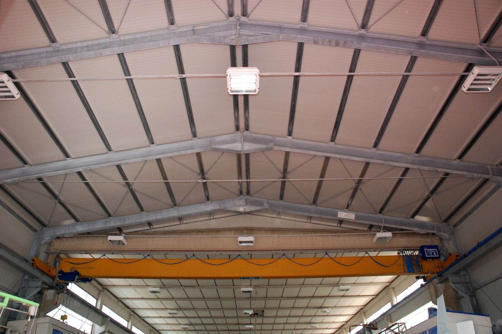 Soffitto di un magazzino industriale con gru a ponte e trave di sollevamento arancione.
