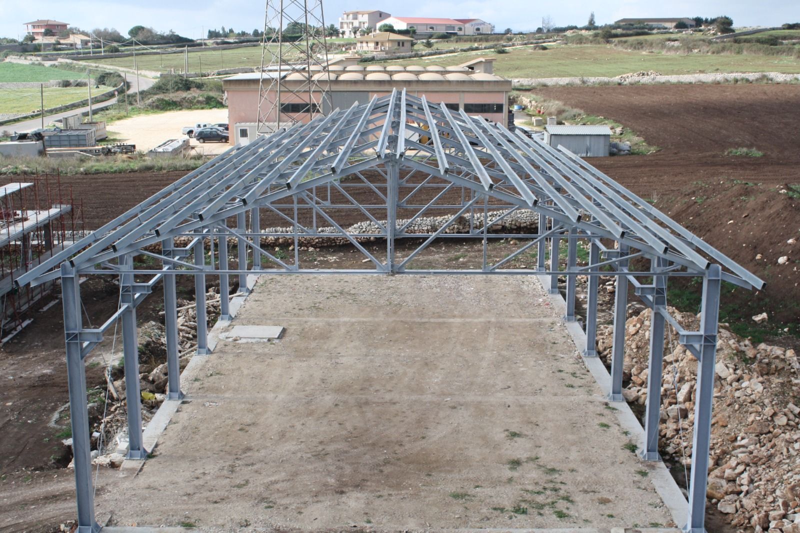 Capriate in acciaio su fondamenta in cemento in un cantiere rurale sotto un cielo sereno
