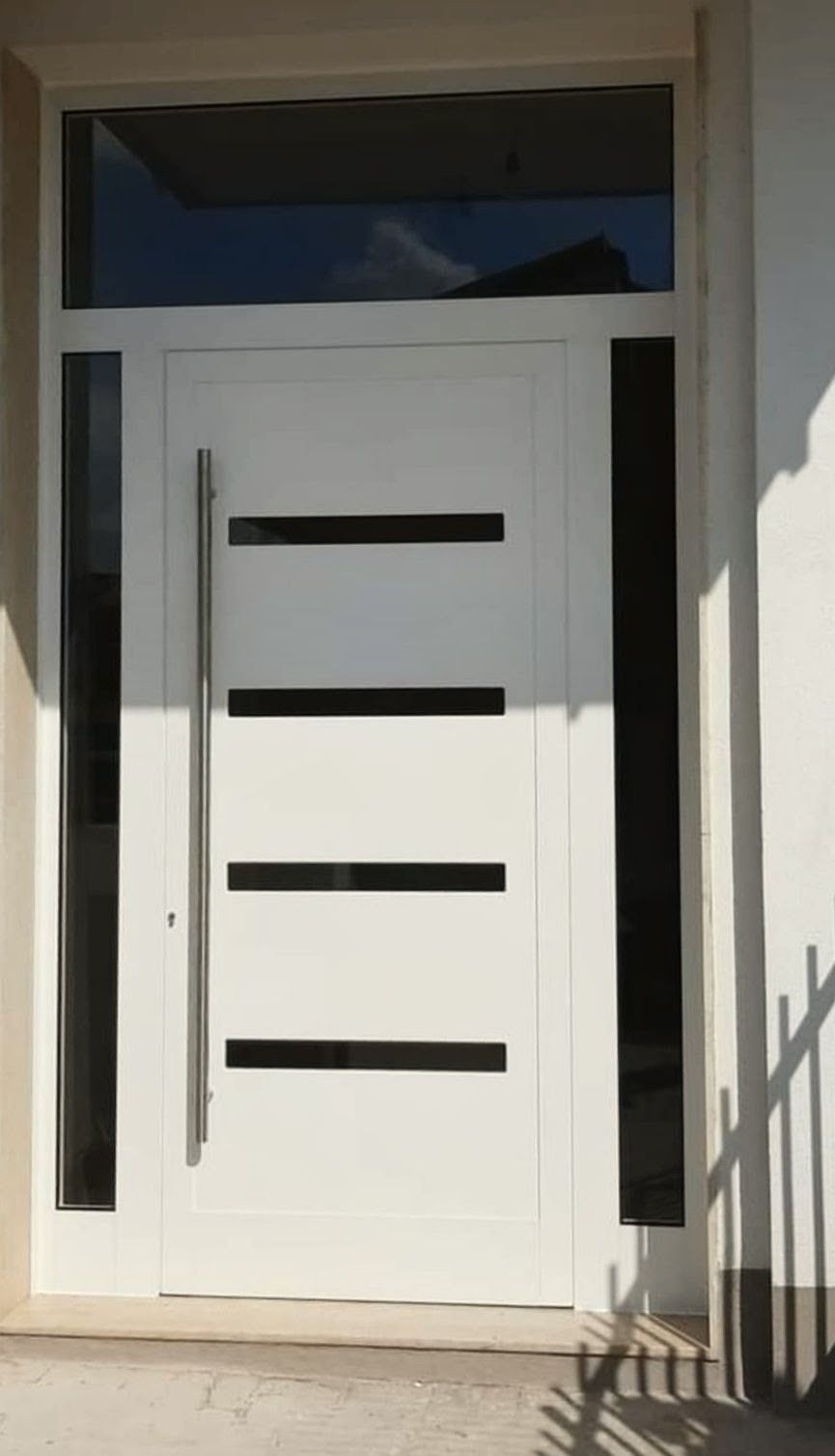 Porta d'ingresso bianca con tre pannelli orizzontali neri e strette finestre laterali sotto una piccola finestra a lunetta.