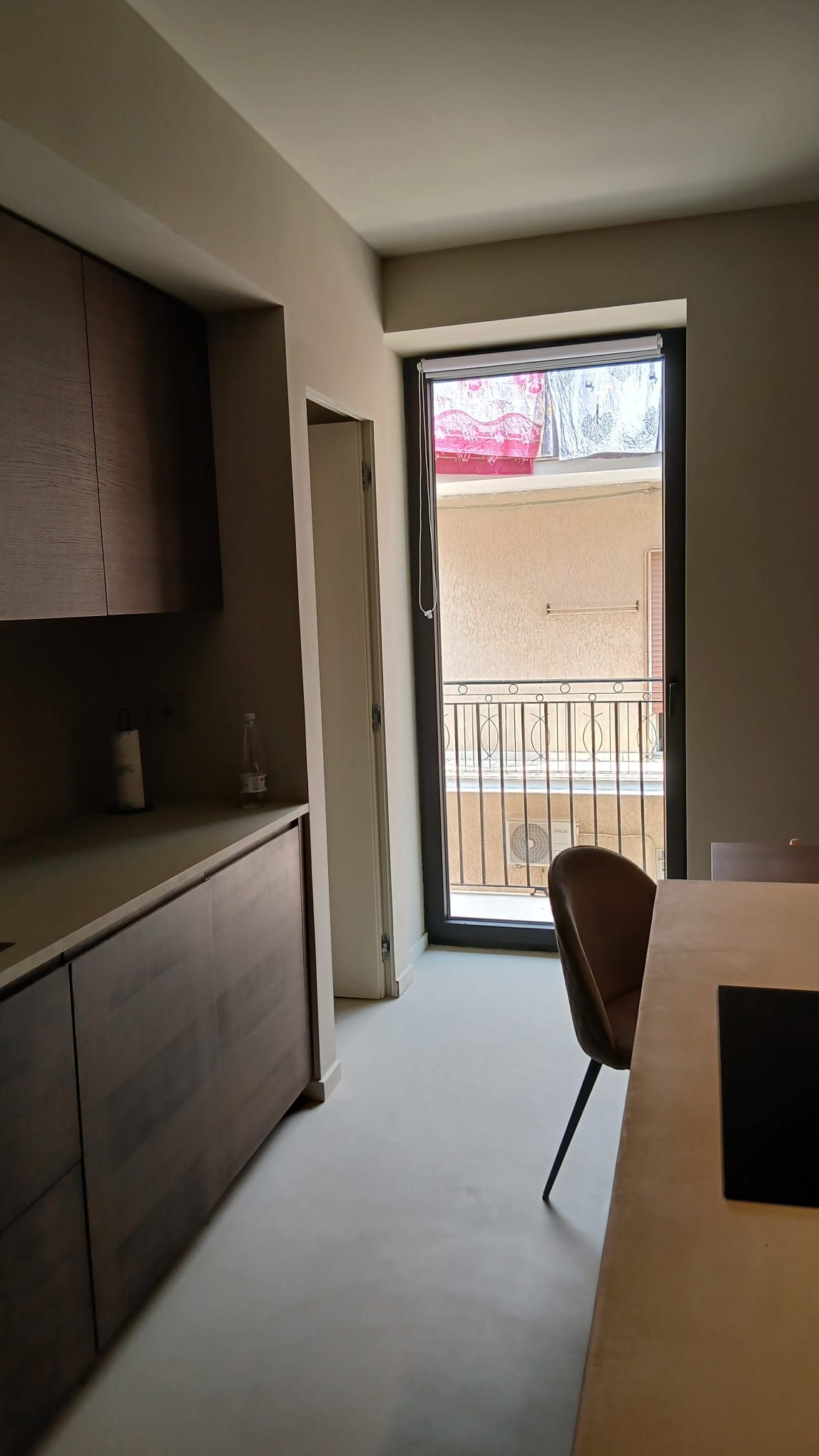 Stretto corridoio con armadietti, sedia e porta aperta su un piccolo balcone o patio.
