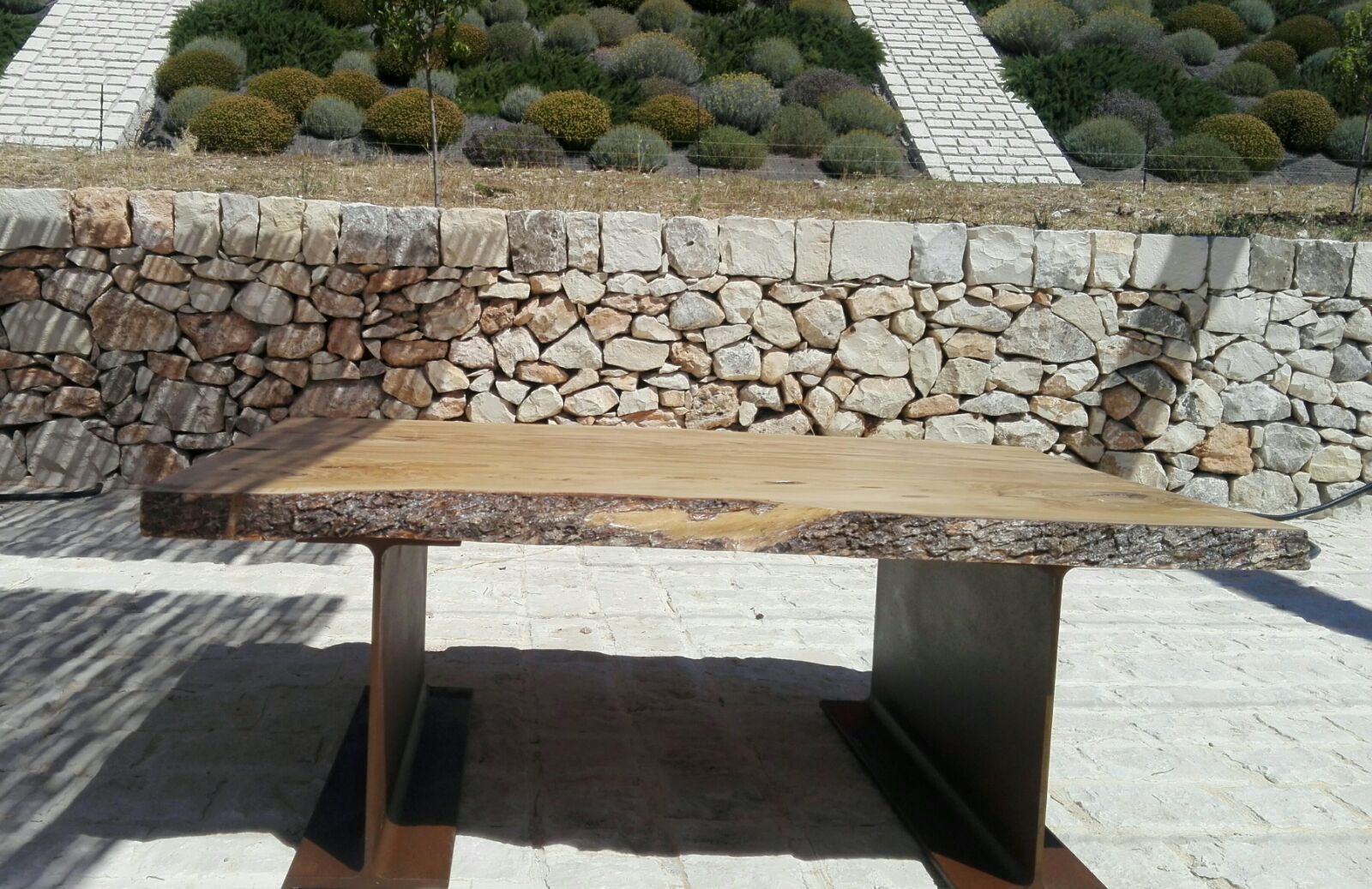 Panchina in pietra in un giardino paesaggistico con sentieri di ghiaia e un muro di contenimento in pietra alle sue spalle.