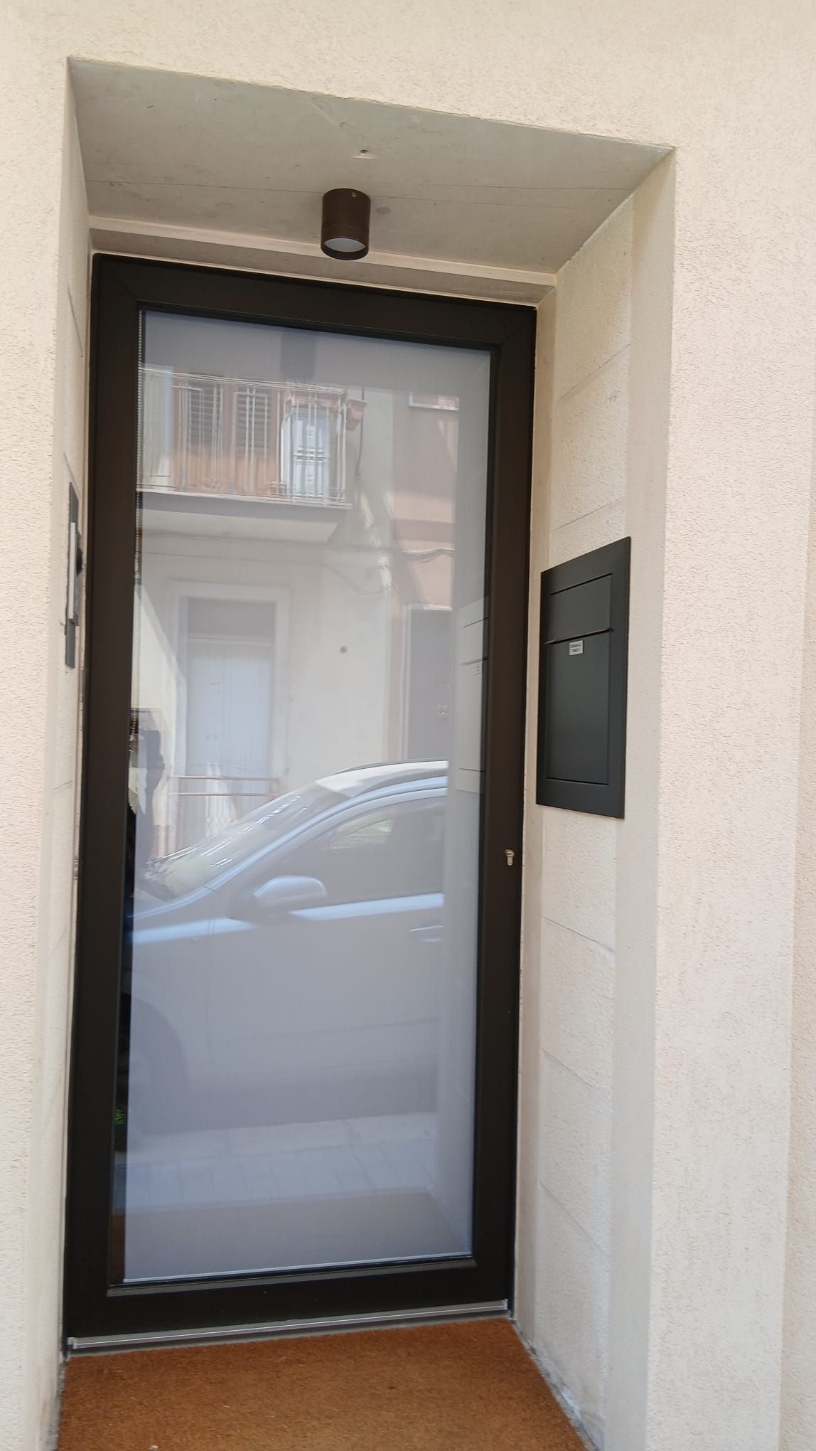 Ingresso principale con porta a vetri con cornice nera e pannello citofonico a parete.
