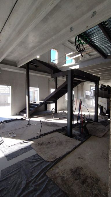 Interno dell'edificio danneggiato con scala crollata, detriti e travi in ​​cemento a vista in uno spazio non rifinito.