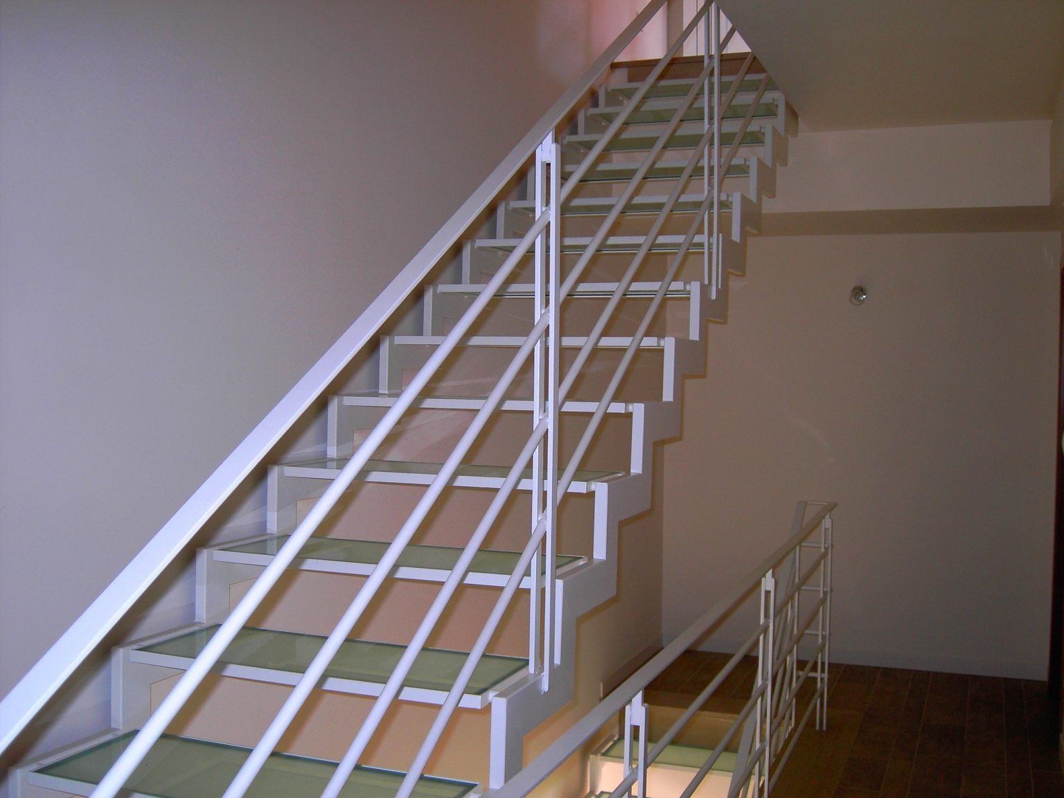 Scala interna con ringhiere bianche e pareti beige che conduce al piano superiore.