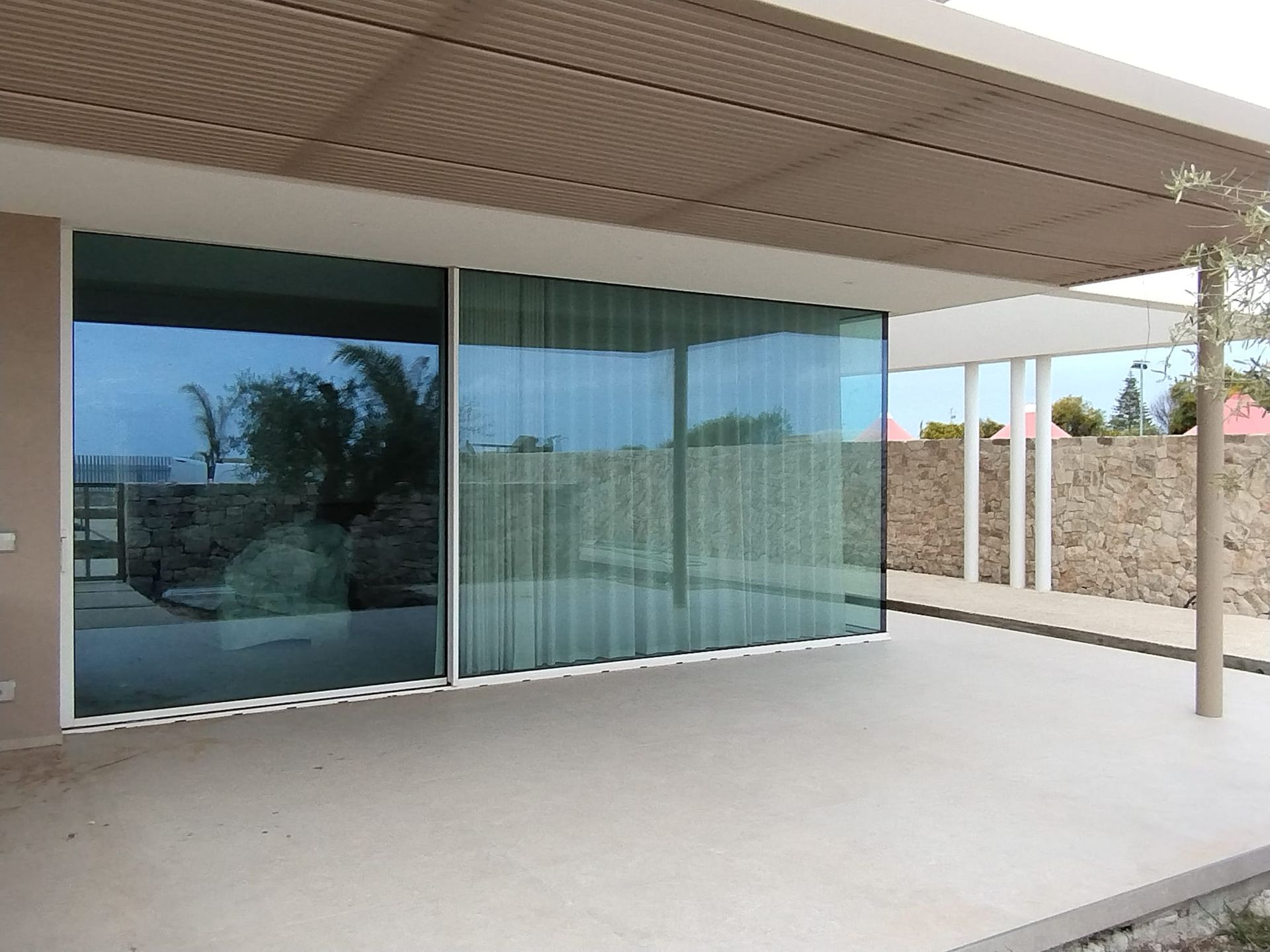 Patio moderno con ampie porte scorrevoli in vetro, tettoia piastrellata e zona esterna coperta in cemento.