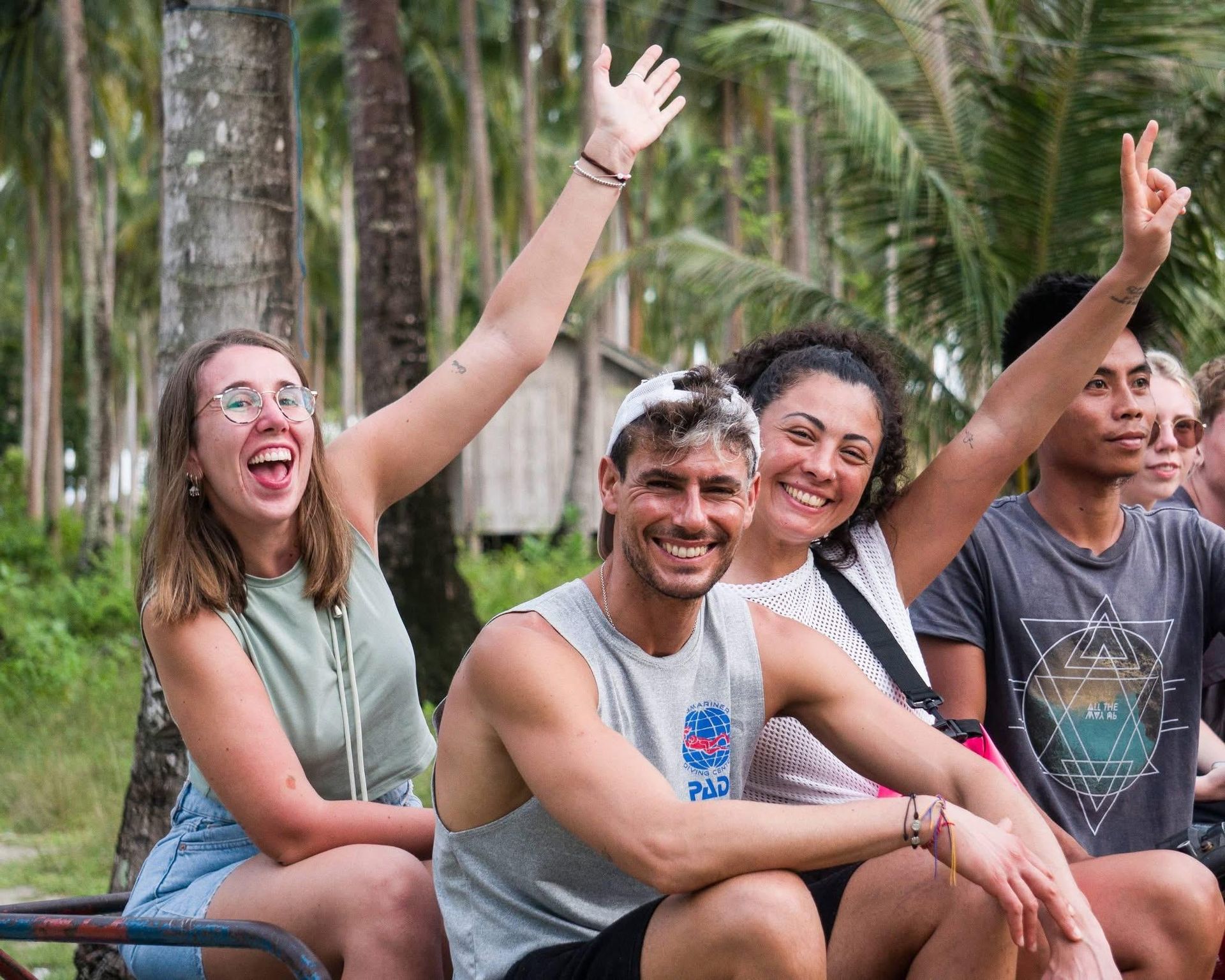 Smiling group of friends outdoors, waving with raised hands in a tropical setting