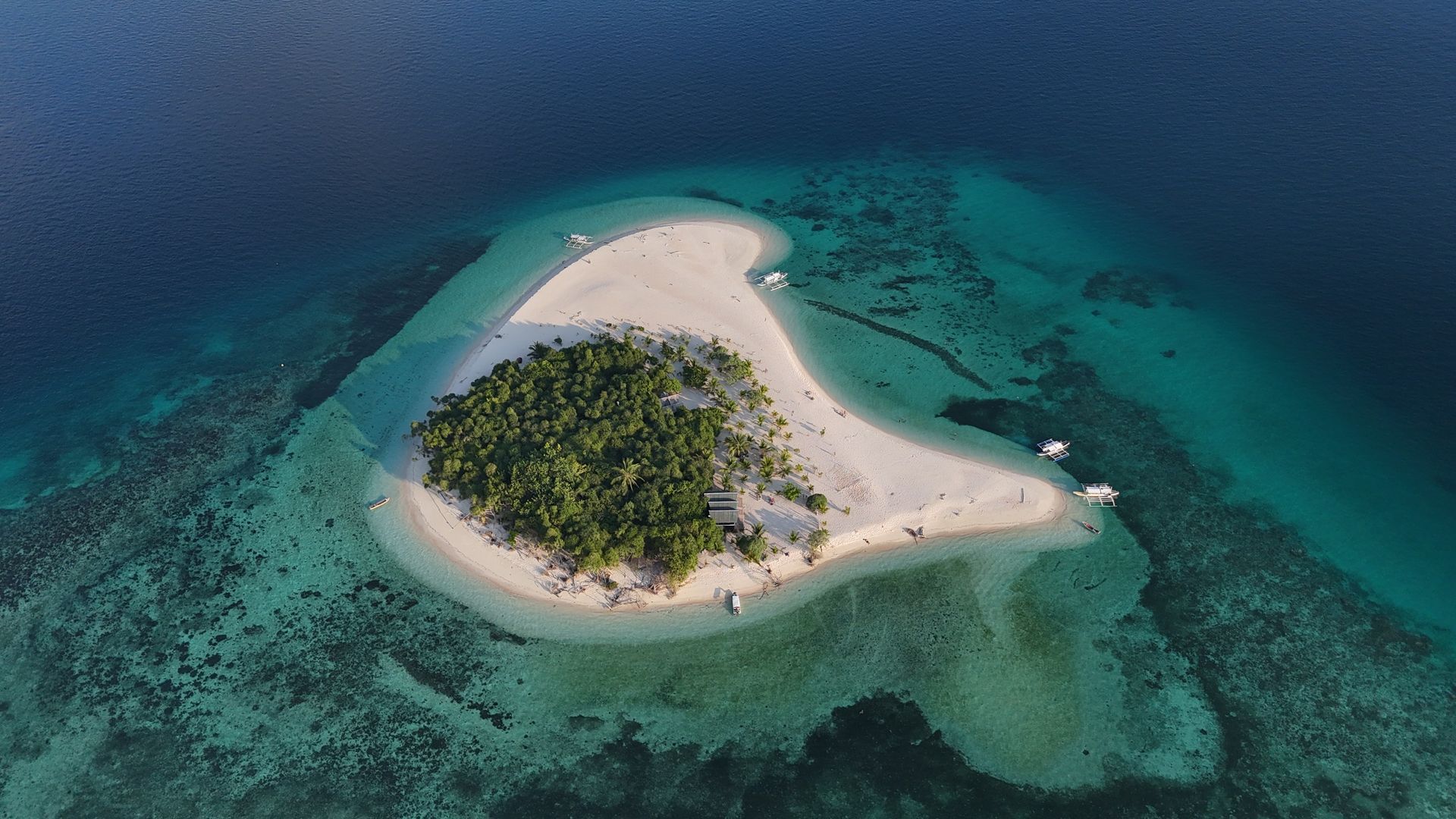 Aerial view of a white sand beach with turquoise water, a small boat, and palm trees along the shore