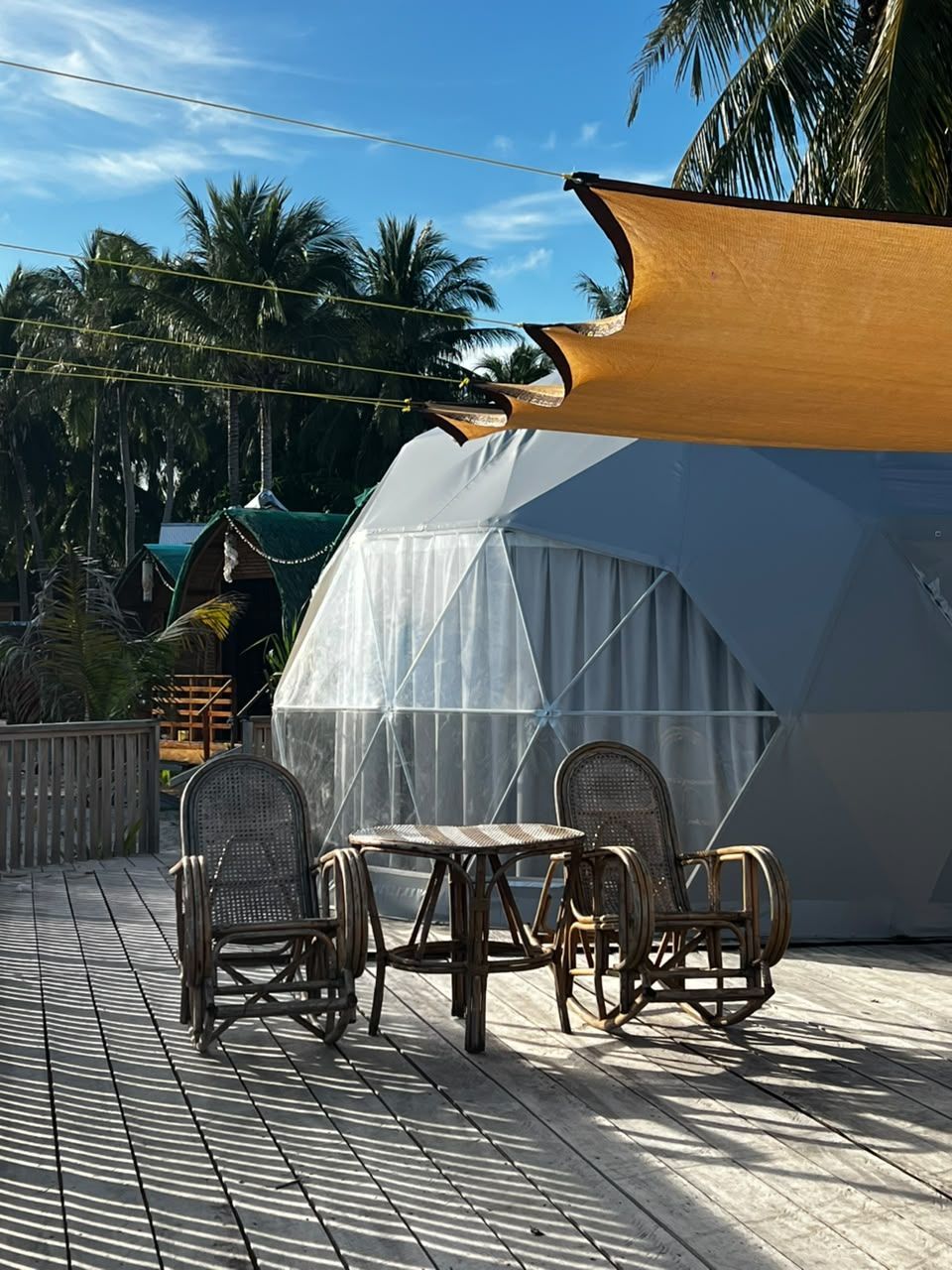 Geodesic dome on a beach under trees, with turquoise water and blue sky in the background