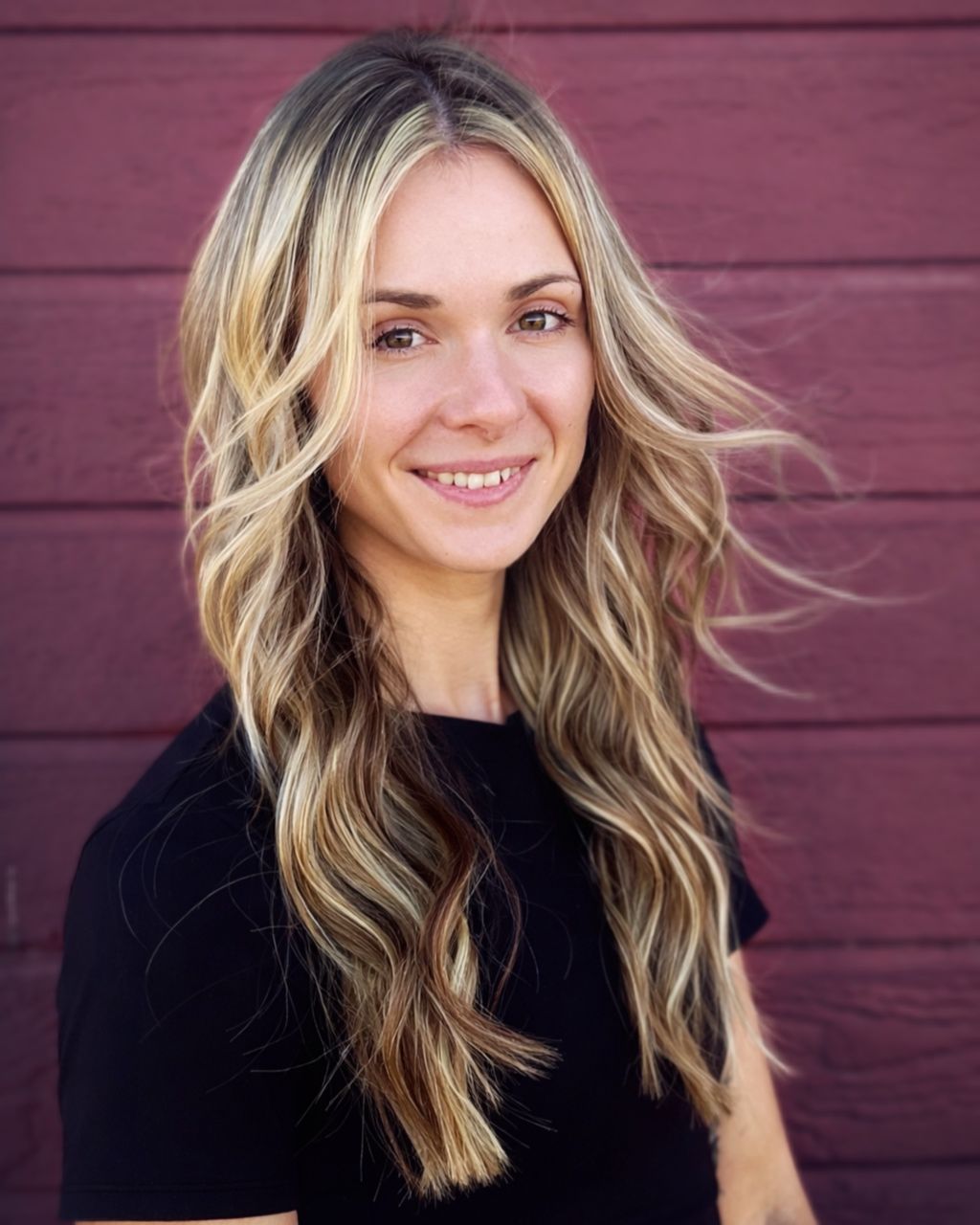 A black-and-white portrait of a person with long, flowing hair, smiling softly against a horizontally paneled background.