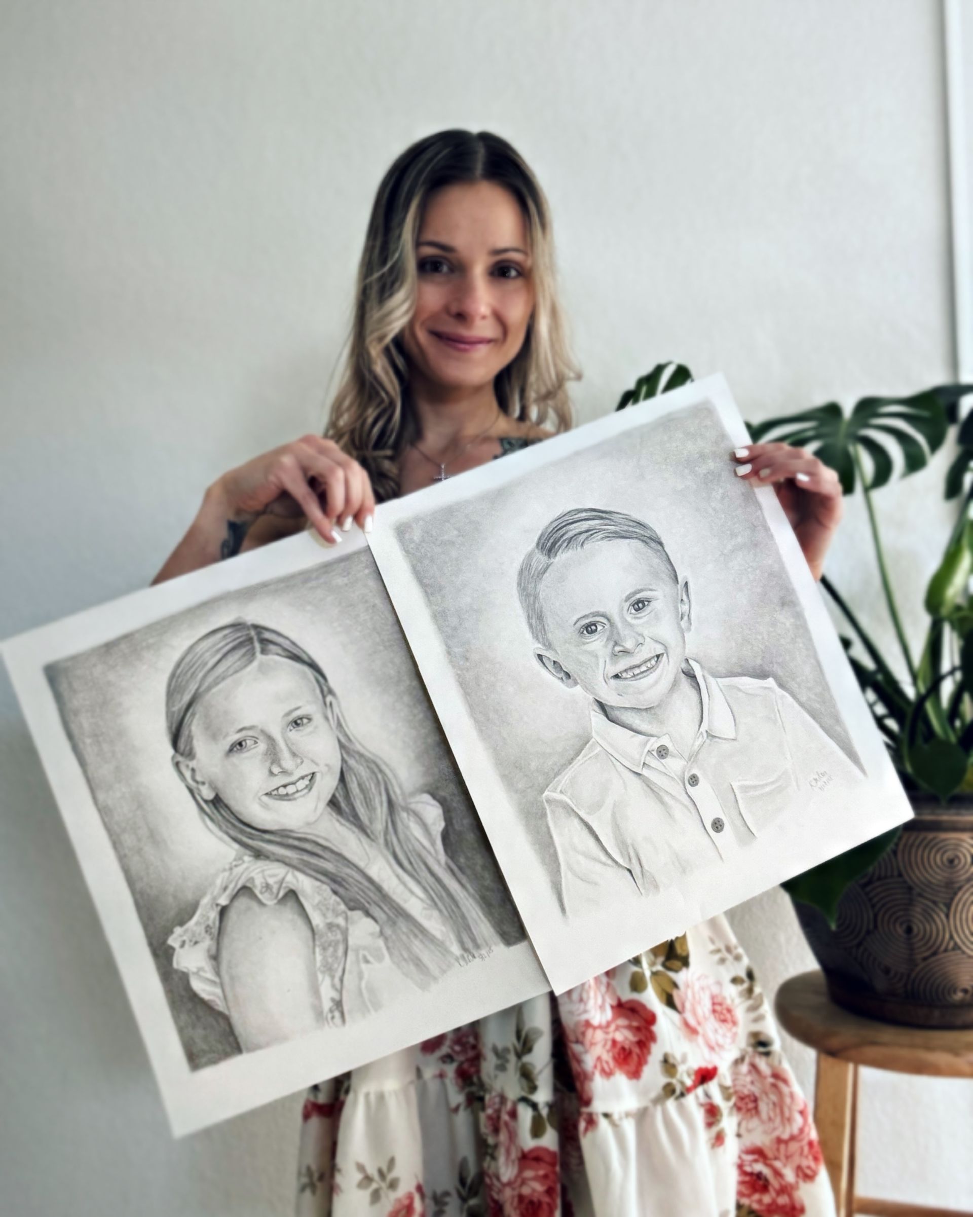 Woman holding two pencil portrait drawings in a bright room
