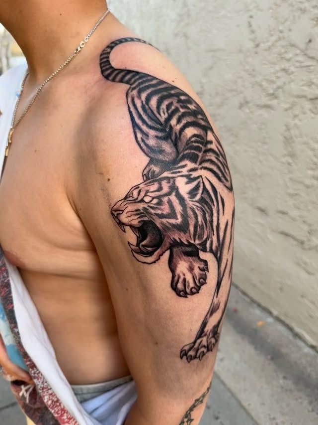 Black tiger tattoo on upper arm and shoulder, with the tiger leaping down the arm.