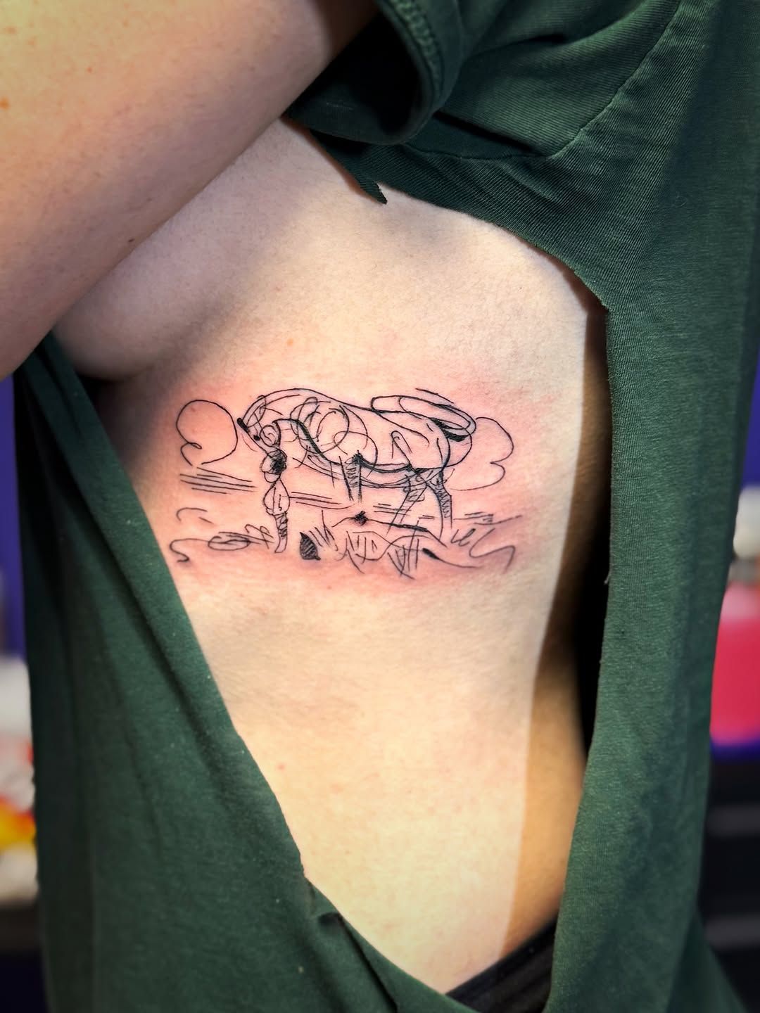 A detailed line-art tattoo on a ribcage depicting two figures embracing within a stylized cloud formation.