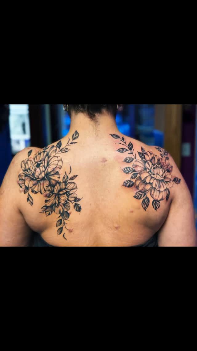 Two floral tattoos on the back of a person, symmetrically placed over each shoulder blade.