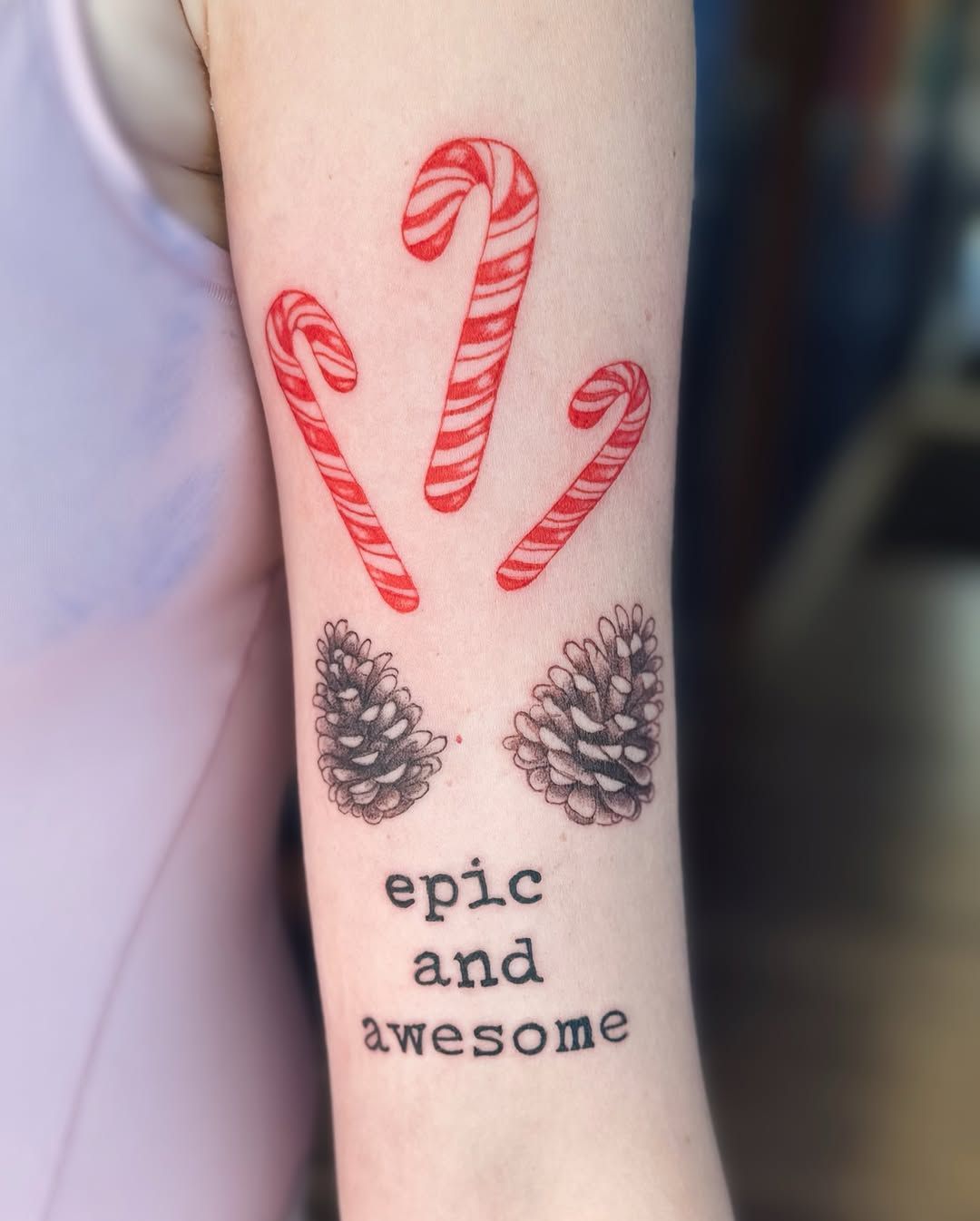 A tattoo on an arm showing three red-and-white candy canes above two pinecones and the text 