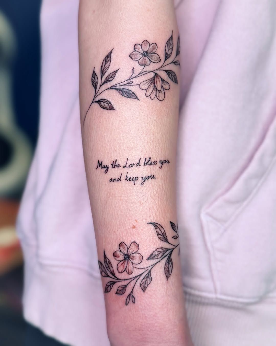 A floral arm tattoo with two vine branches bordering the script: 