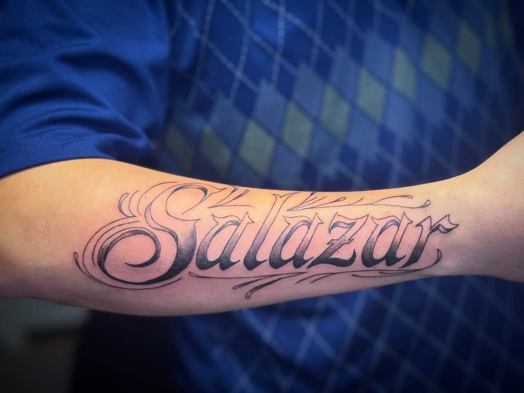 A forearm tattoo in cursive, black-ink script reads 