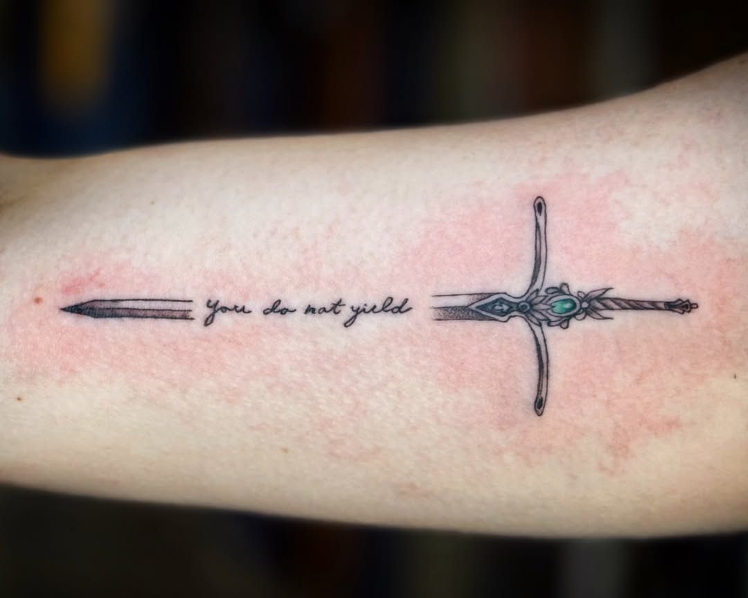 A forearm tattoo of a sword intersected by the handwritten phrase 