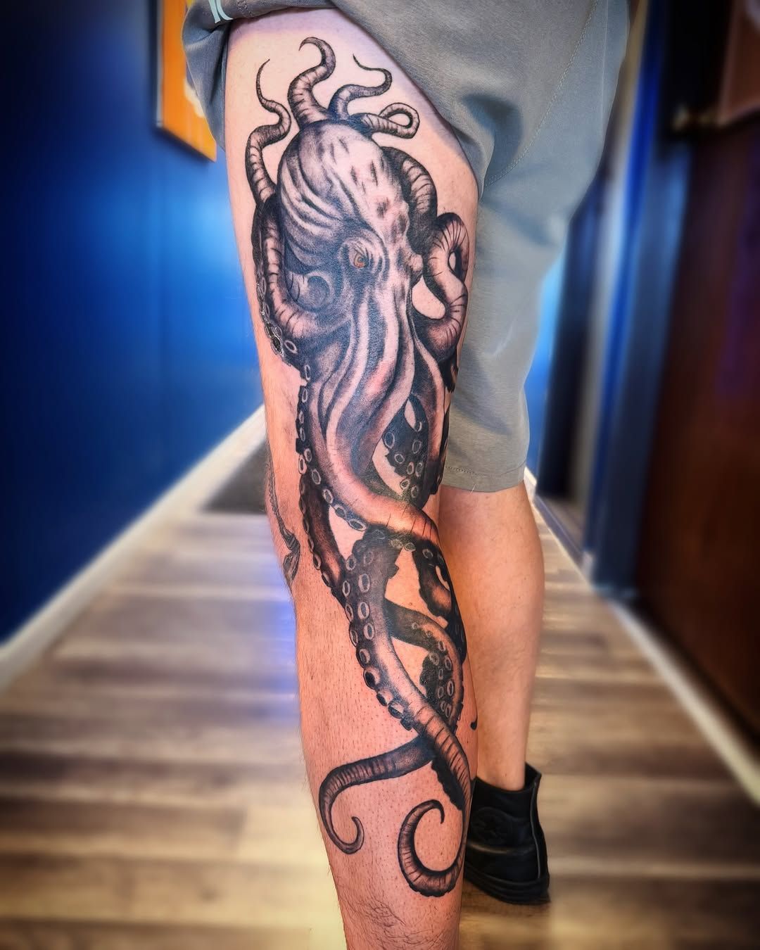 A detailed black-and-grey octopus tattoo extending from the thigh down to the calf of a person’s leg.