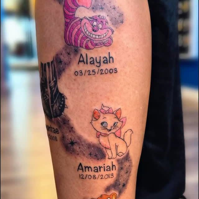 A tattoo featuring cartoon cats with names and dates, connected by a starry, dark trail on skin.