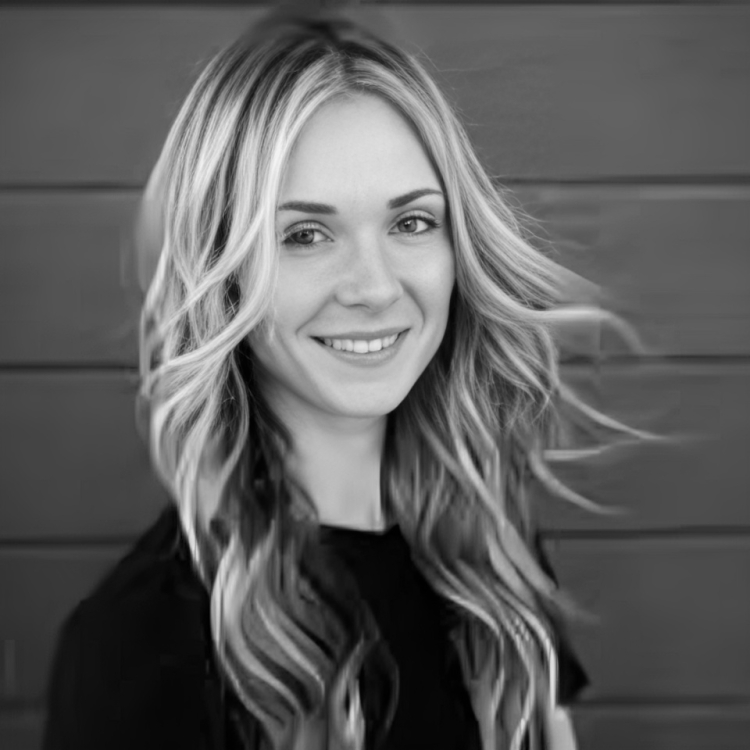 A black-and-white portrait of a person with long, flowing hair, smiling softly against a horizontally paneled background.