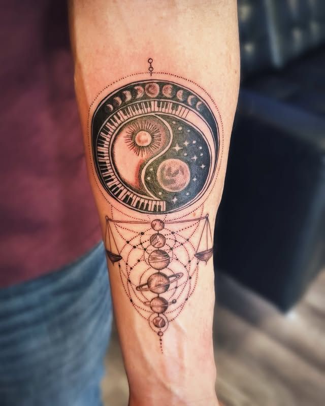 A forearm tattoo featuring a yin-yang sun and moon design surrounded by moon phases above a geometric solar system diagram.