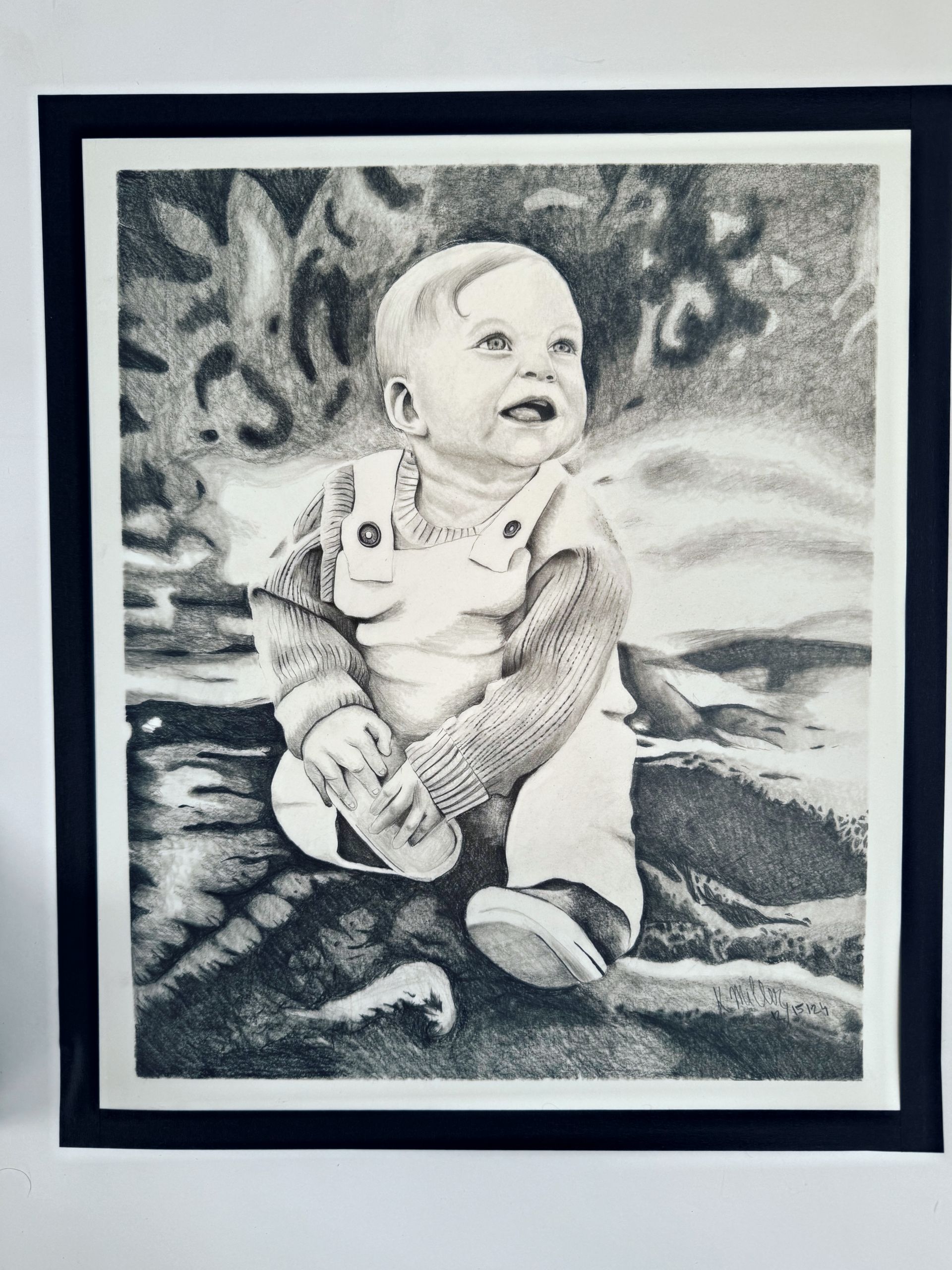 Black-and-white portrait of a smiling baby sitting on a patterned blanket.