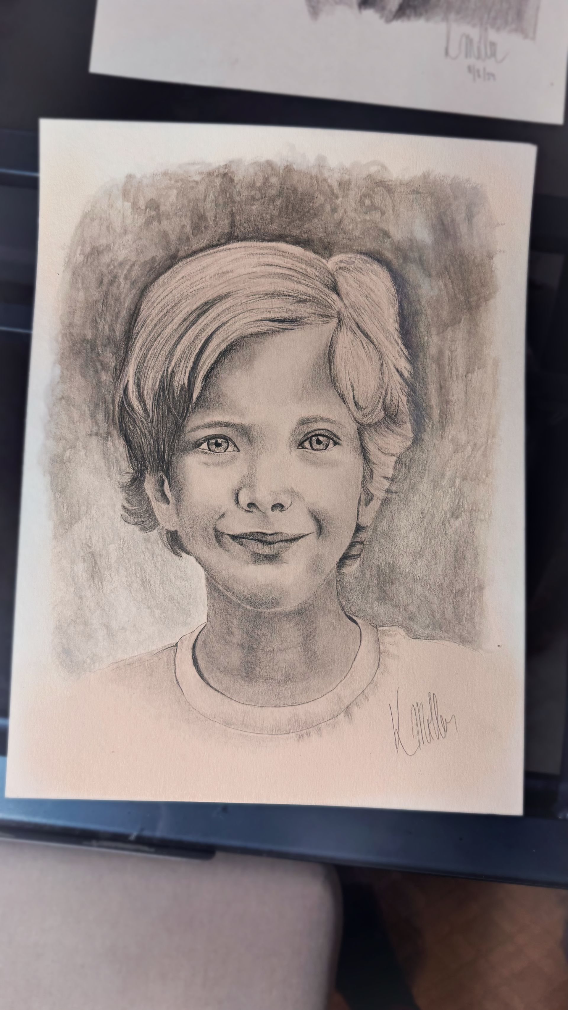Pencil portrait sketch of a smiling person with short hair on a sheet of paper.