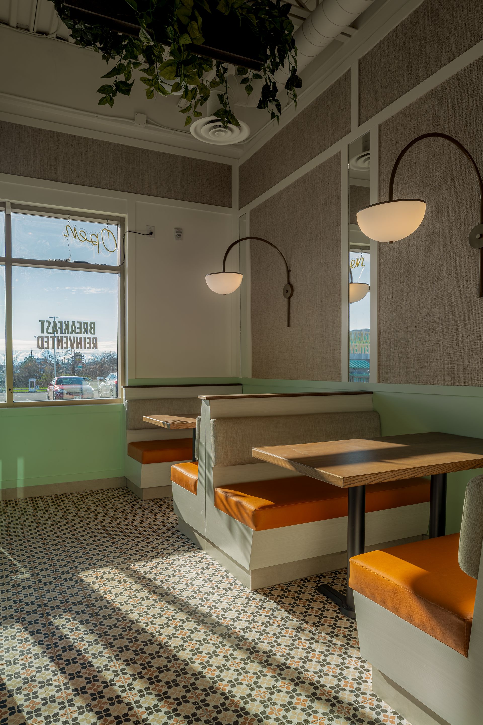 A retro diner interior with orange booths, patterned flooring, and natural light shining through a window.