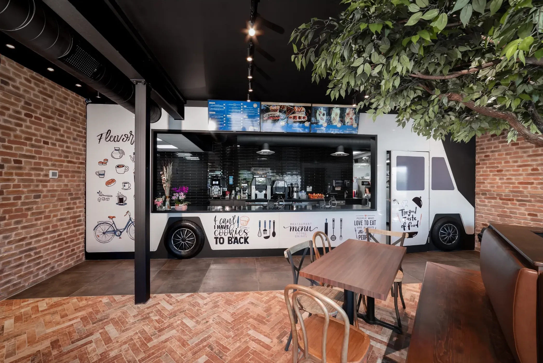 Interior of a restaurant with a food truck design. Tables and chairs are in front of the truck, which has a counter and windows.