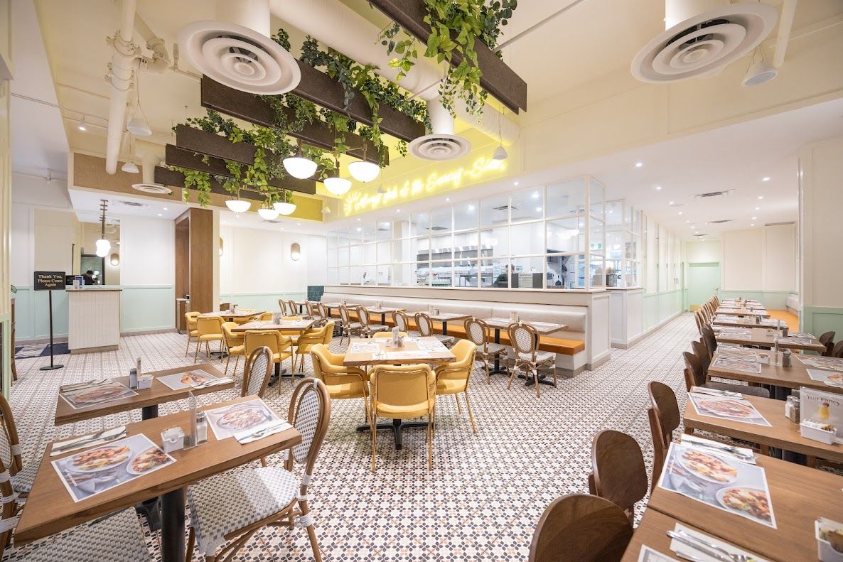 Restaurant interior with patterned tile floor, yellow chairs, and hanging greenery. A bright, inviting space.