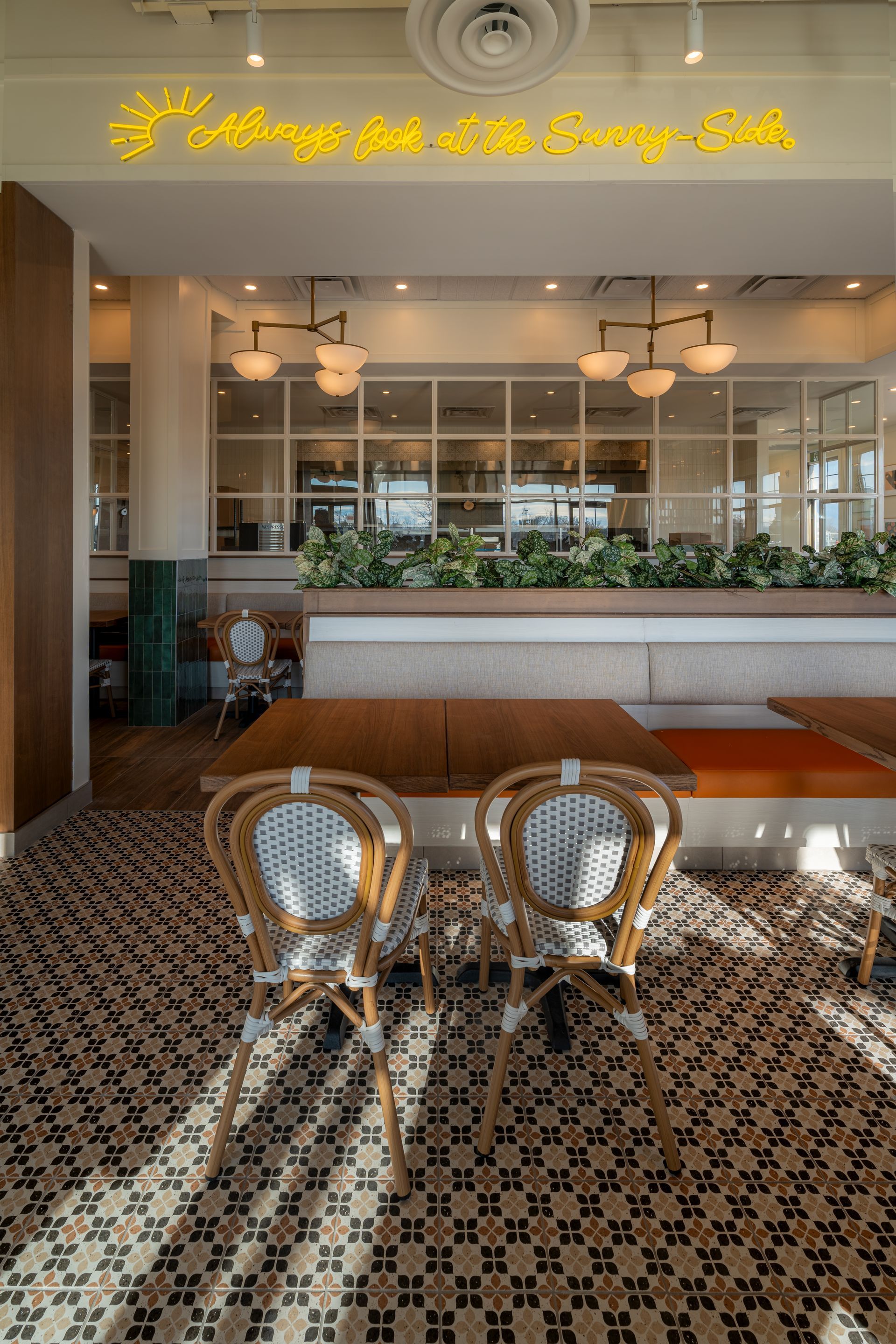 Interior view of a restaurant with two rattan chairs, a tiled floor, and a neon sign that reads,