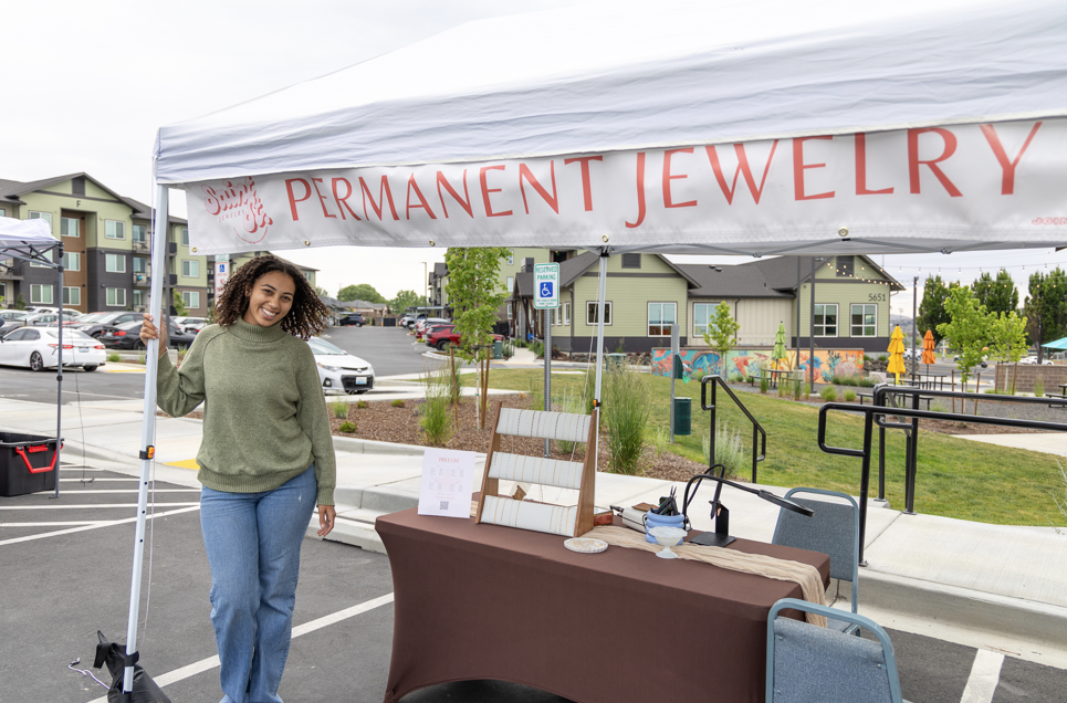 Woman standing in front of community market table with various jewelry